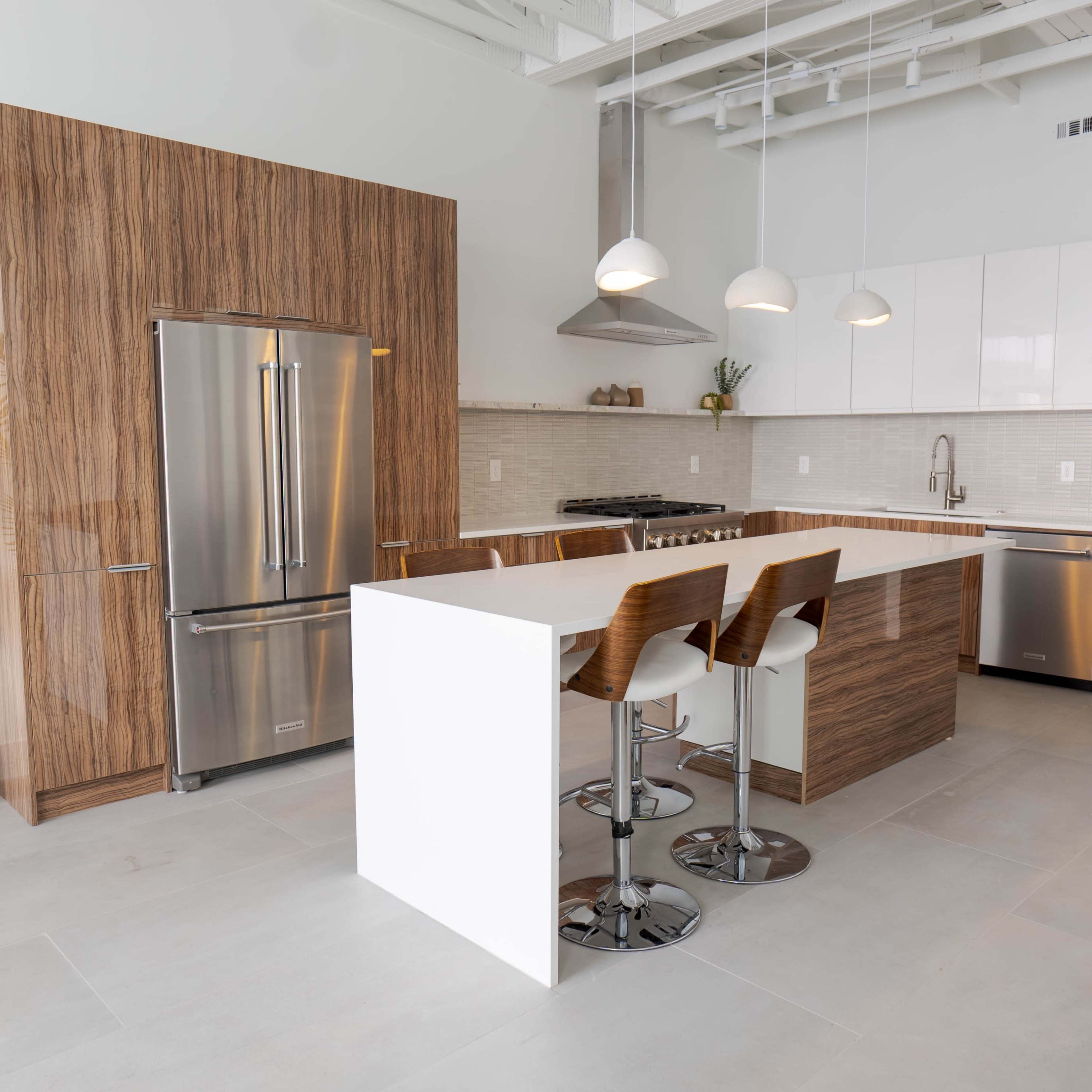 A modern kitchen with a refrigerator and cabinets made of wood and white materials, a central island with seating, and a potted plant in the corner.