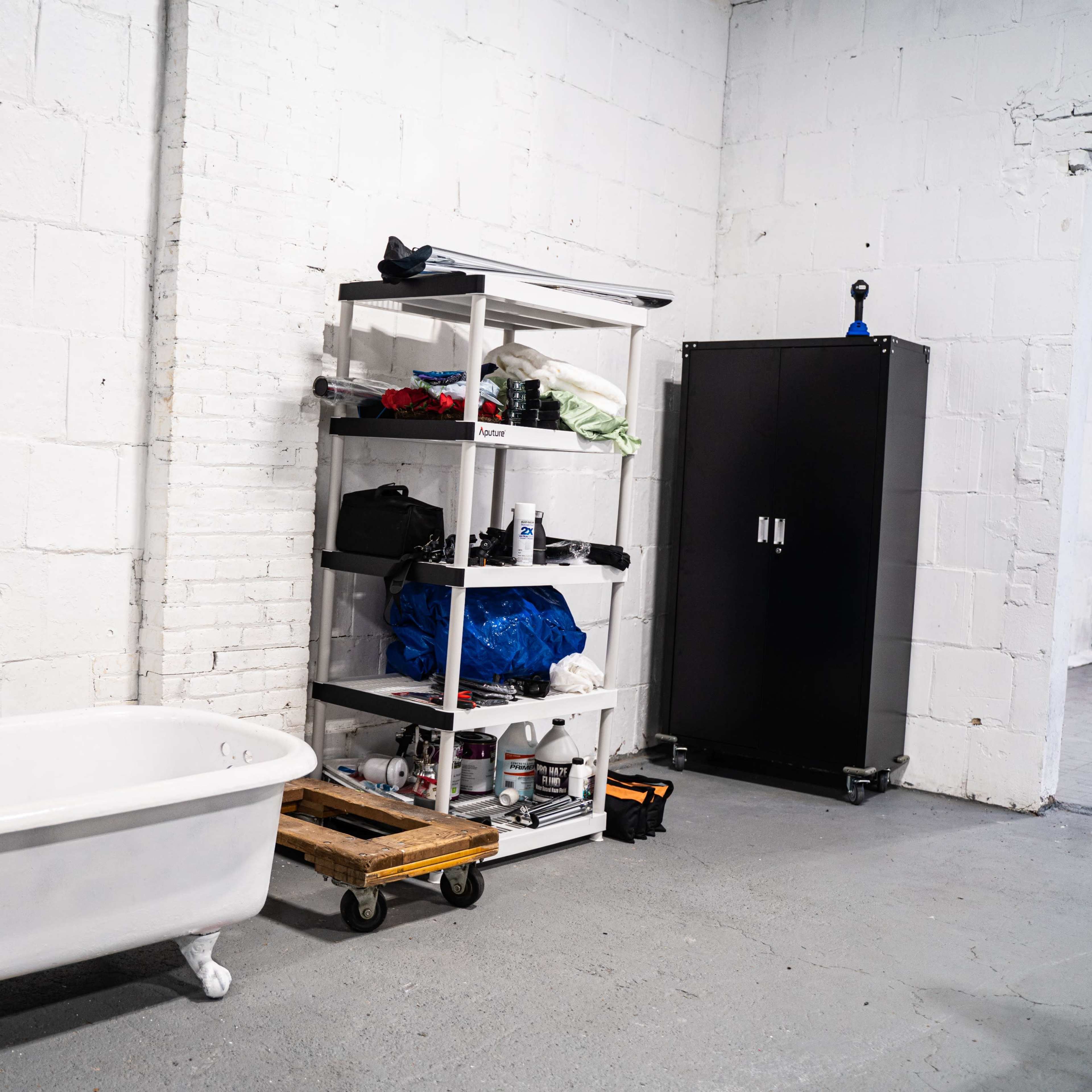 A white clawfoot bathtub beside a metal shelving unit filled with various items in an industrial-style room with white brick walls.