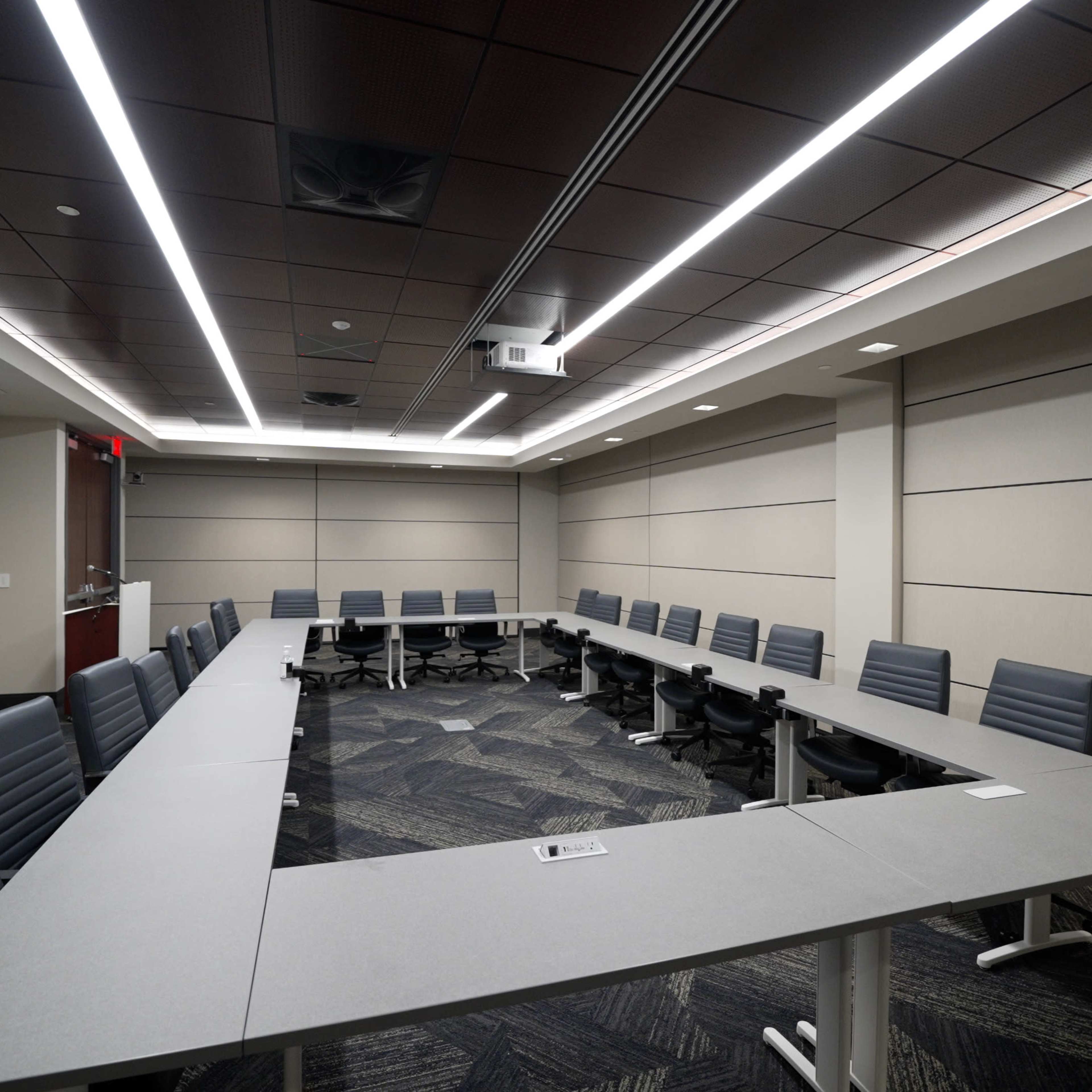 A modern conference room arranged with a long table surrounded by black office chairs and equipped with a projector screen.