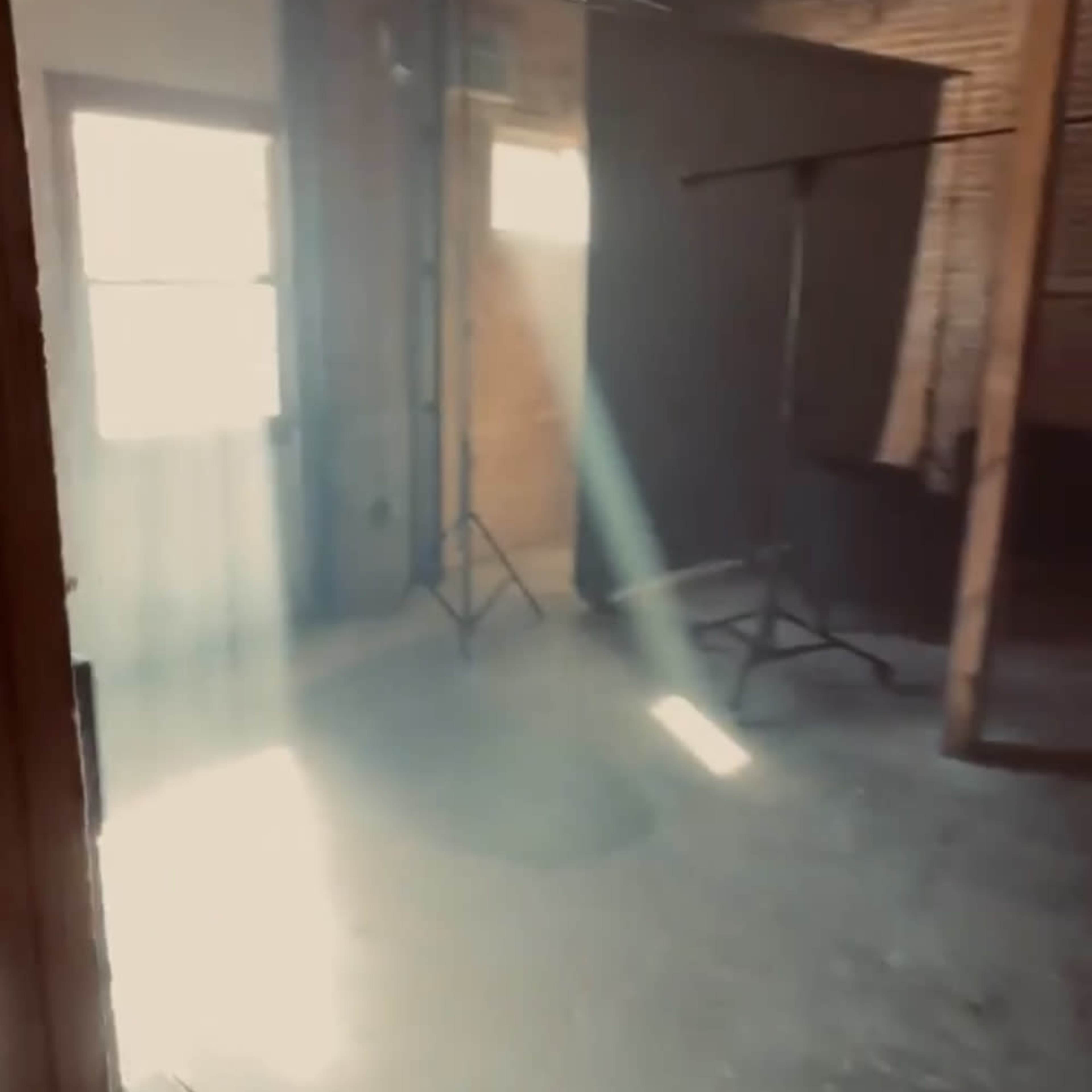 An empty room with wooden walls and beams, featuring a beam of light streaming through a window and casting a shadow on the floor.