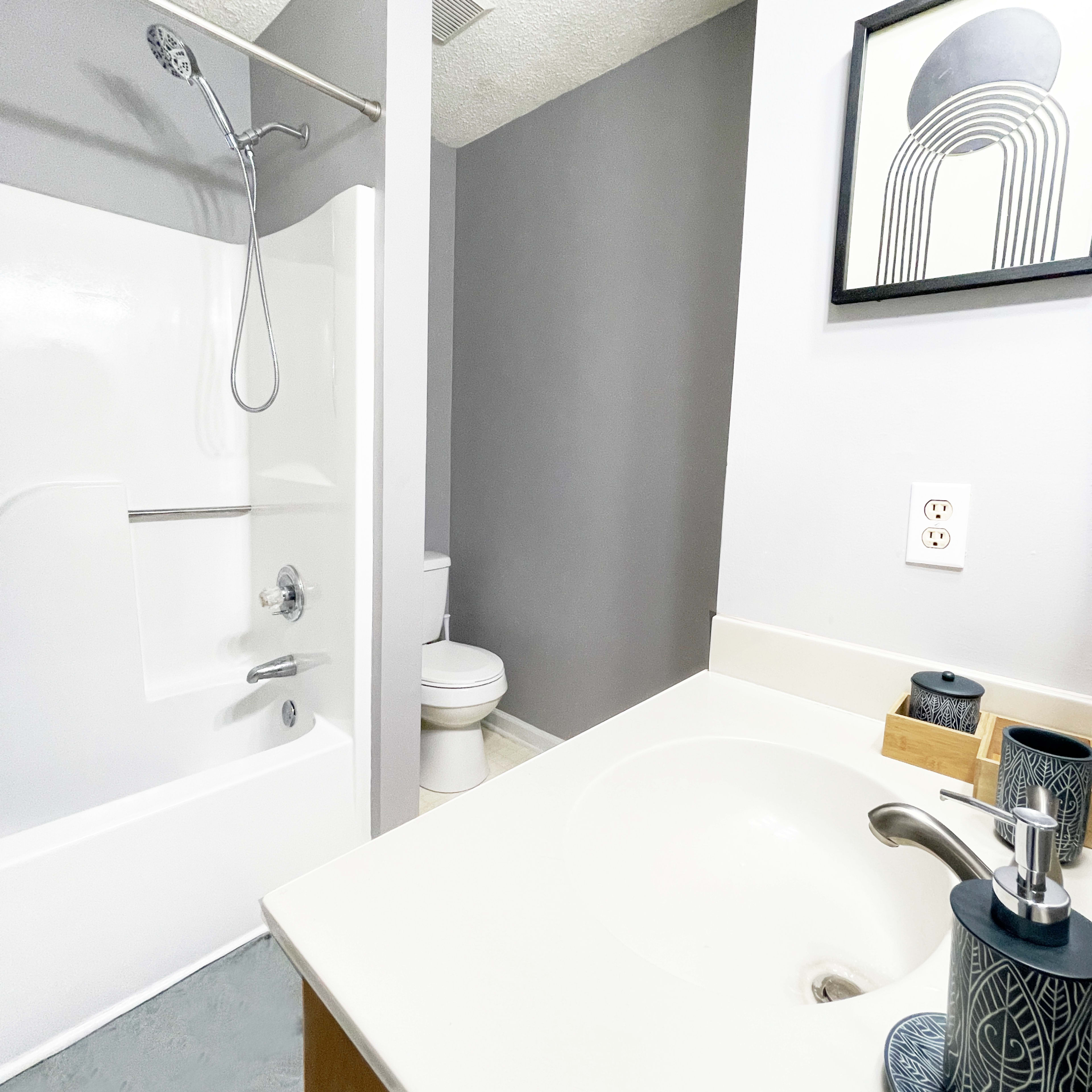 A modern bathroom featuring a shower nook, toilet, and a sink with a countertop.