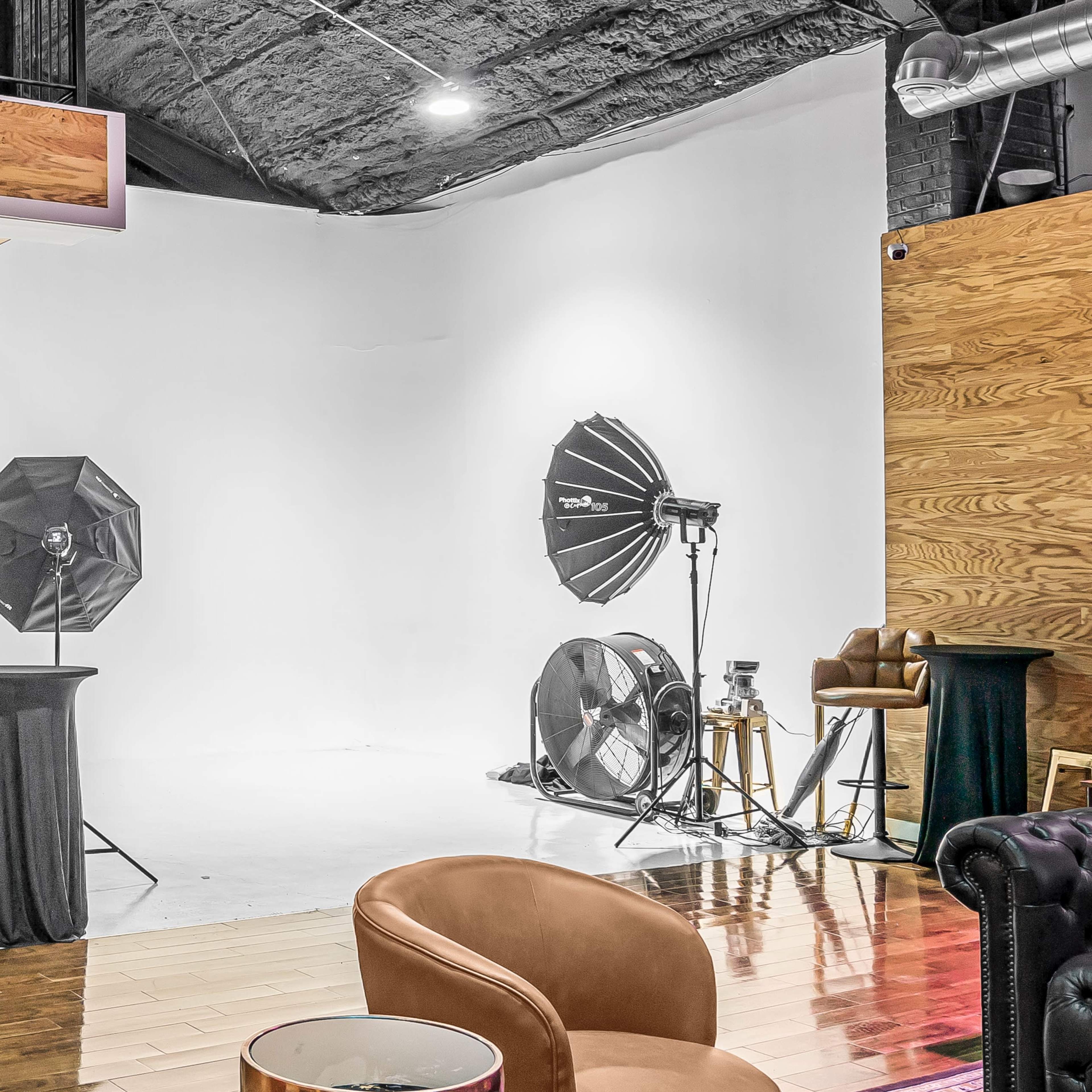 A photography studio with a white backdrop, lighting equipment, and various furniture pieces.
