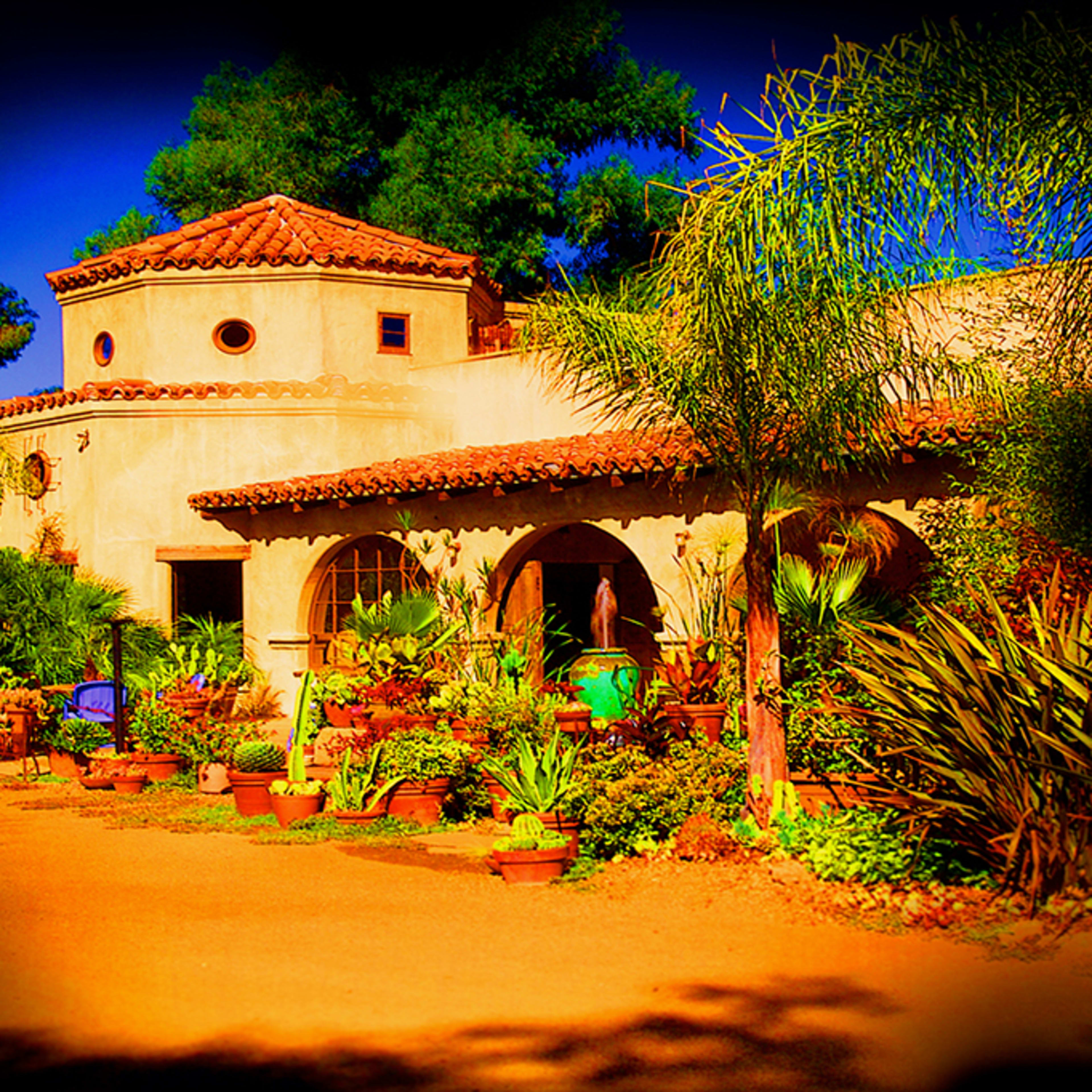A rustic adobe-style house surrounded by lush greenery and potted plants.