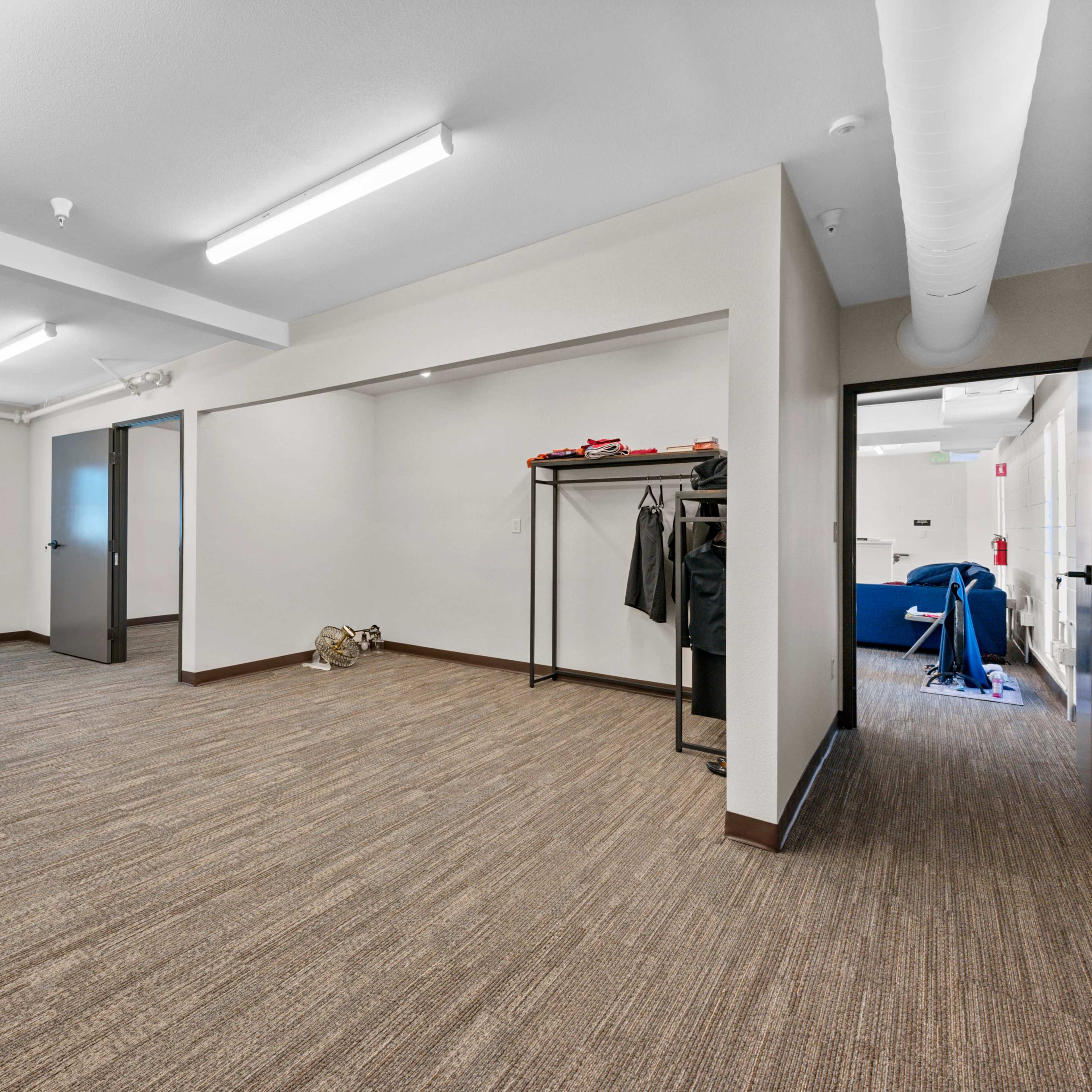 An empty room with beige walls, a light brown carpet, and a clothing rack against one wall.