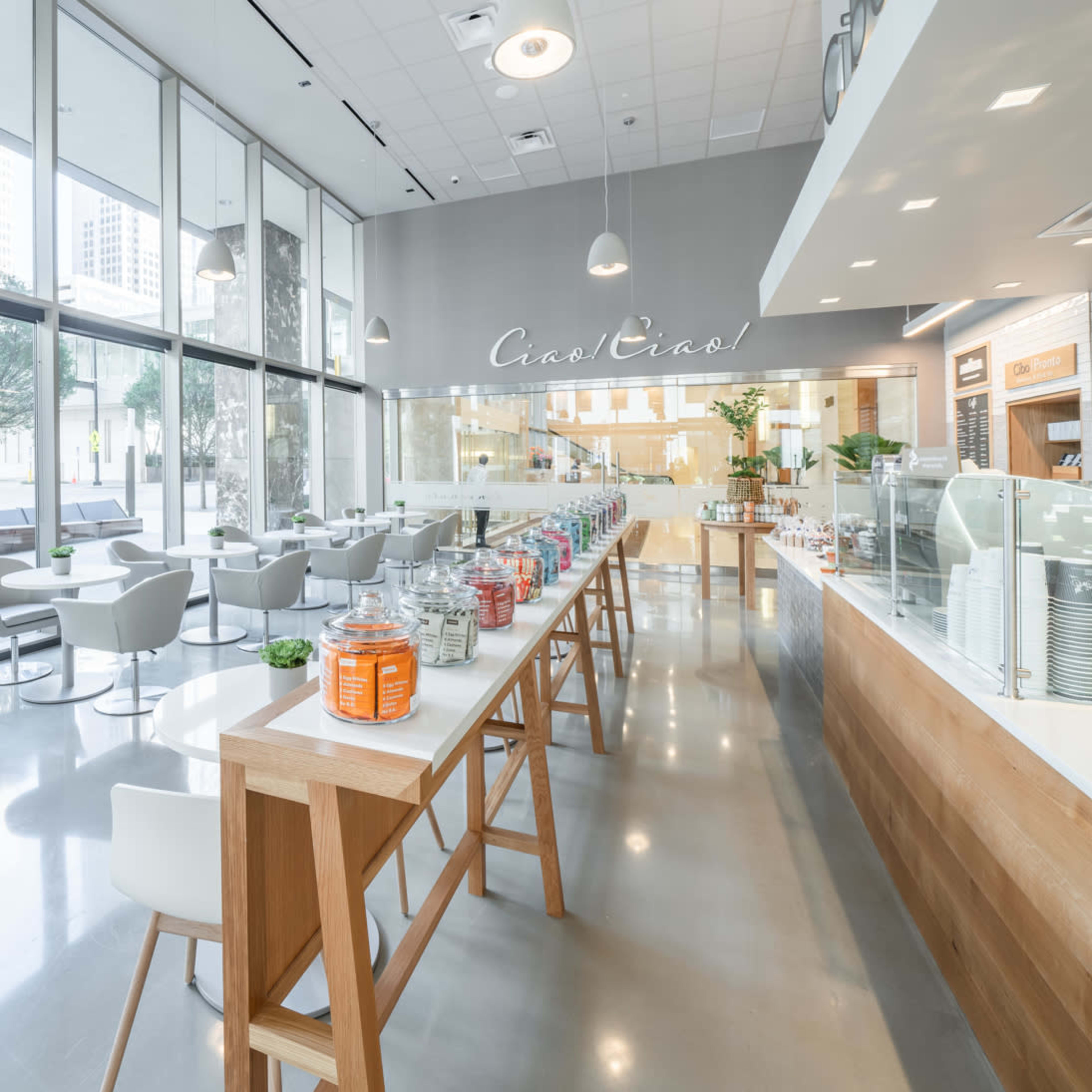 A modern café with large windows, featuring seating areas and a display of jars on a counter.
