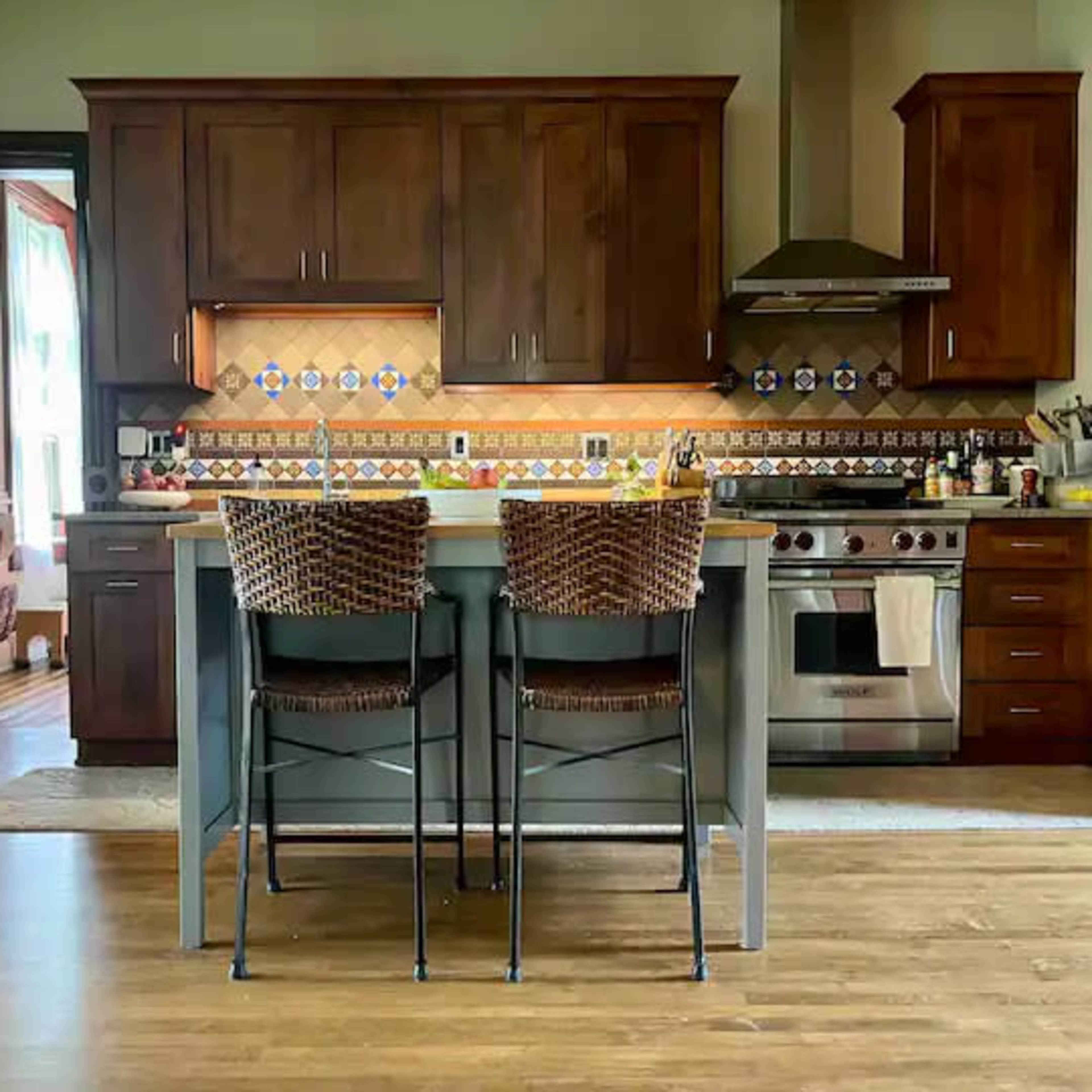 A kitchen with dark wood cabinets, a stainless steel gas range, and two woven bar stools at a central island.