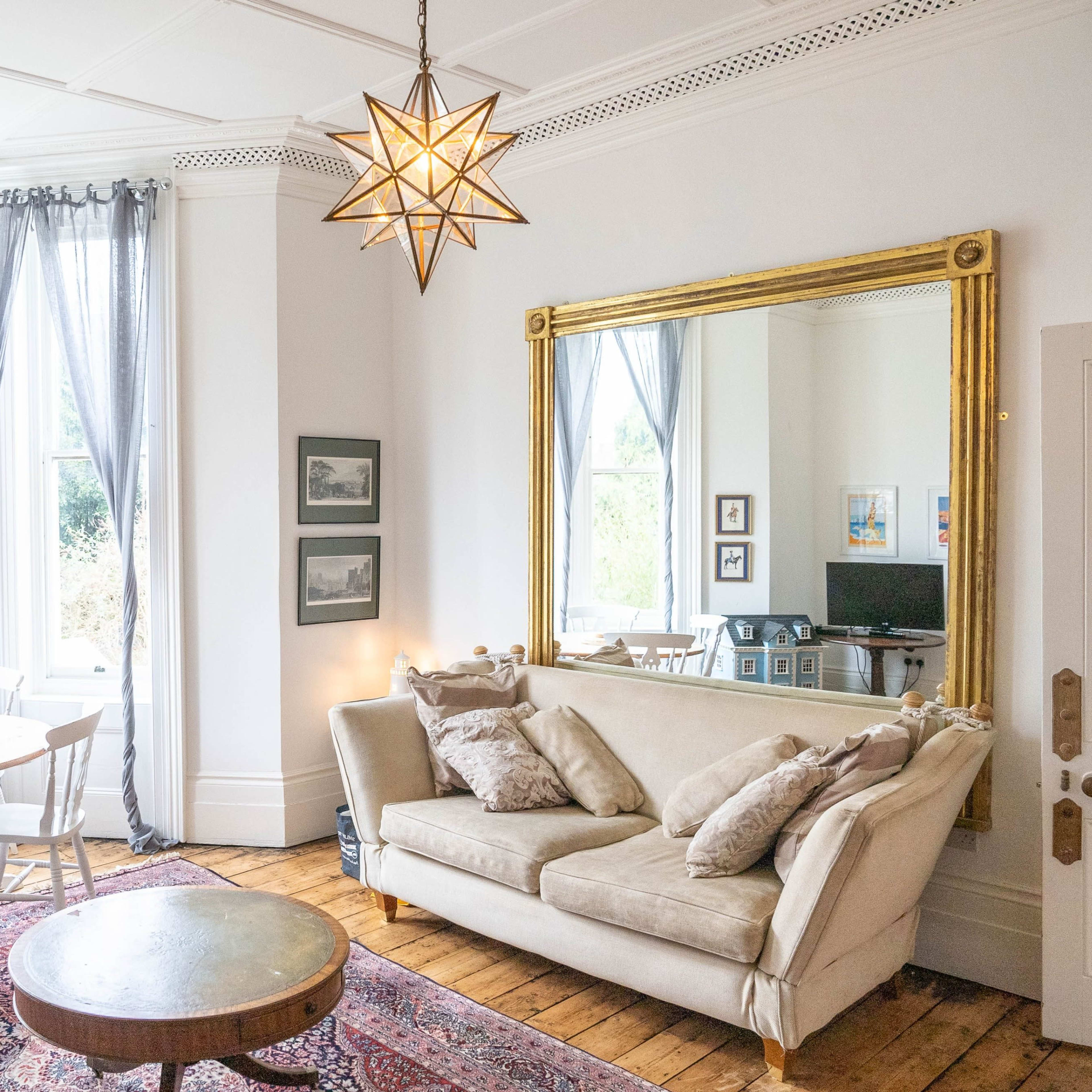 A cozy living room with a beige sofa, a wooden coffee table, a round dining table beside large windows, and a decorative star-shaped ceiling light.
