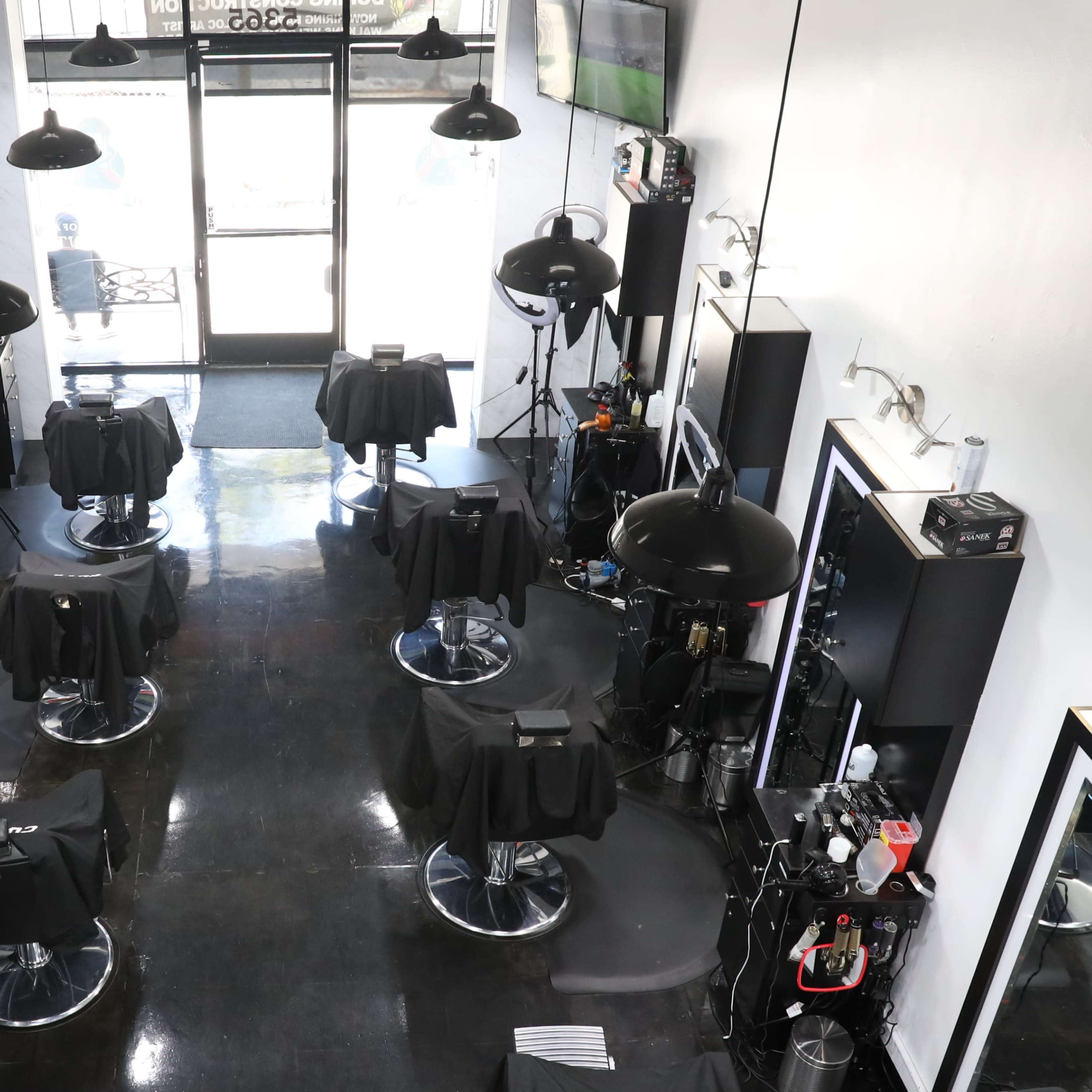 A hair salon interior with several styling stations, each featuring a black salon chair and lighting equipment, arranged in a spacious layout.