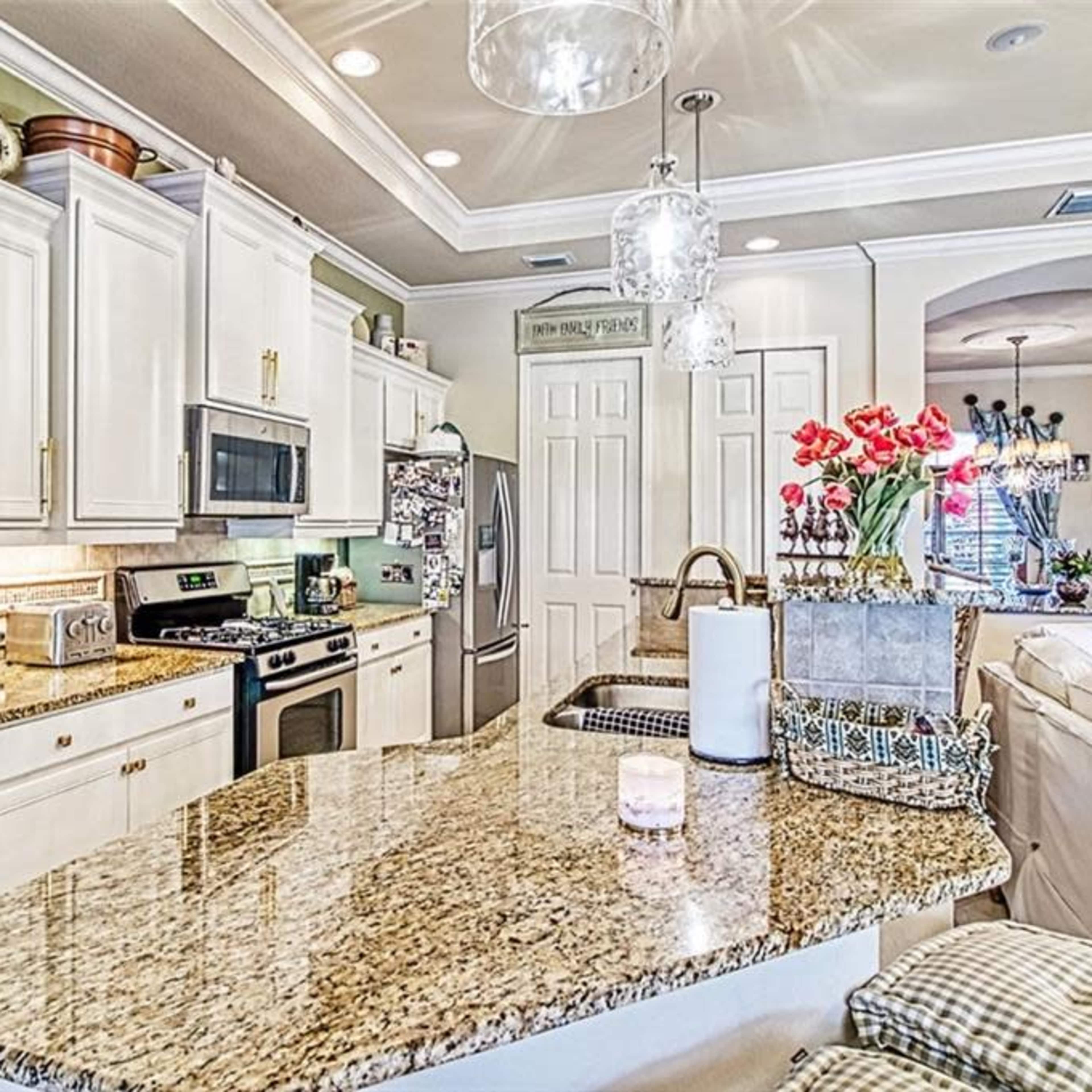 A modern kitchen with white cabinets, a large granite island, and decorative overhead lighting.