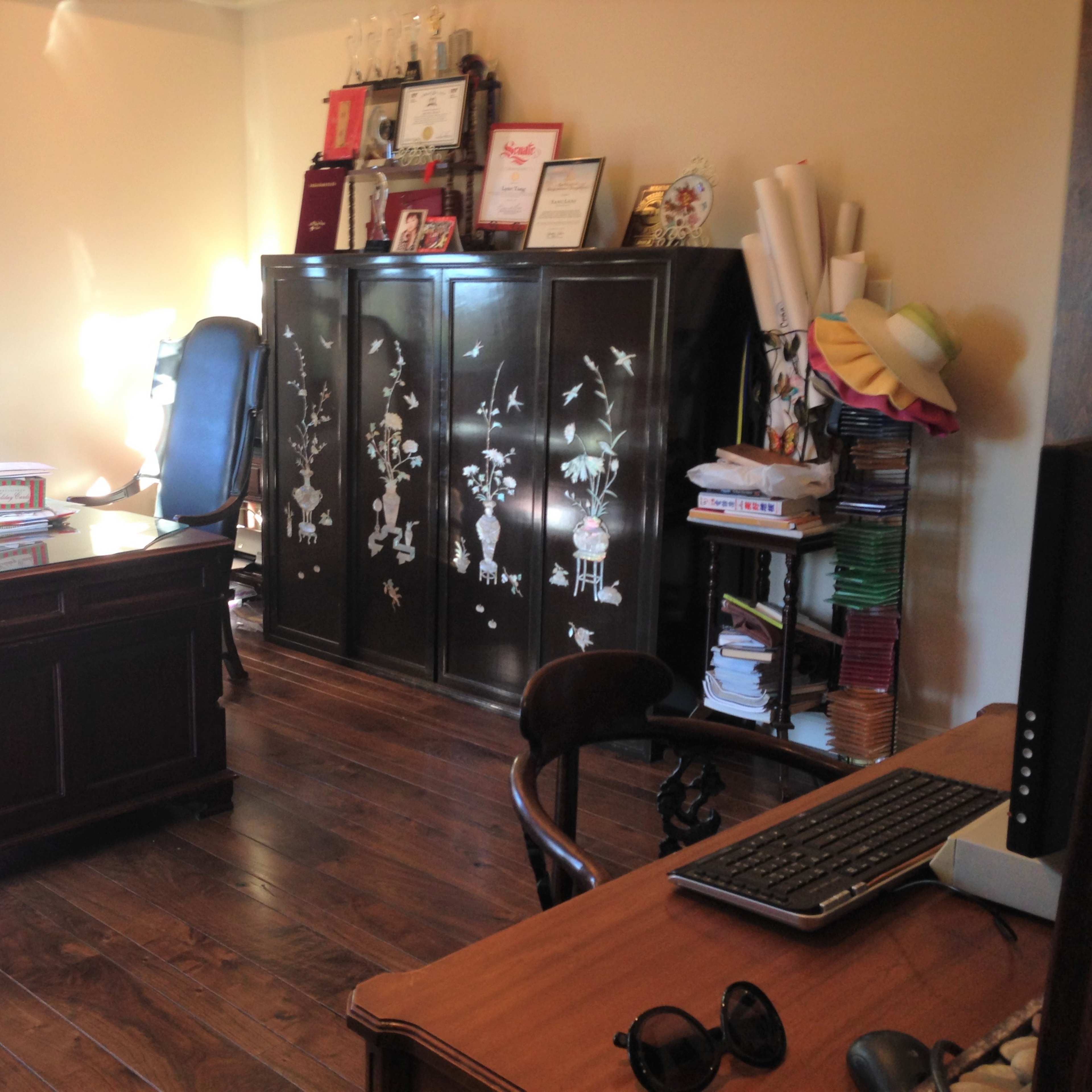 A well-furnished office with two desks, a black cabinet decorated with floral designs, and shelves filled with various items.