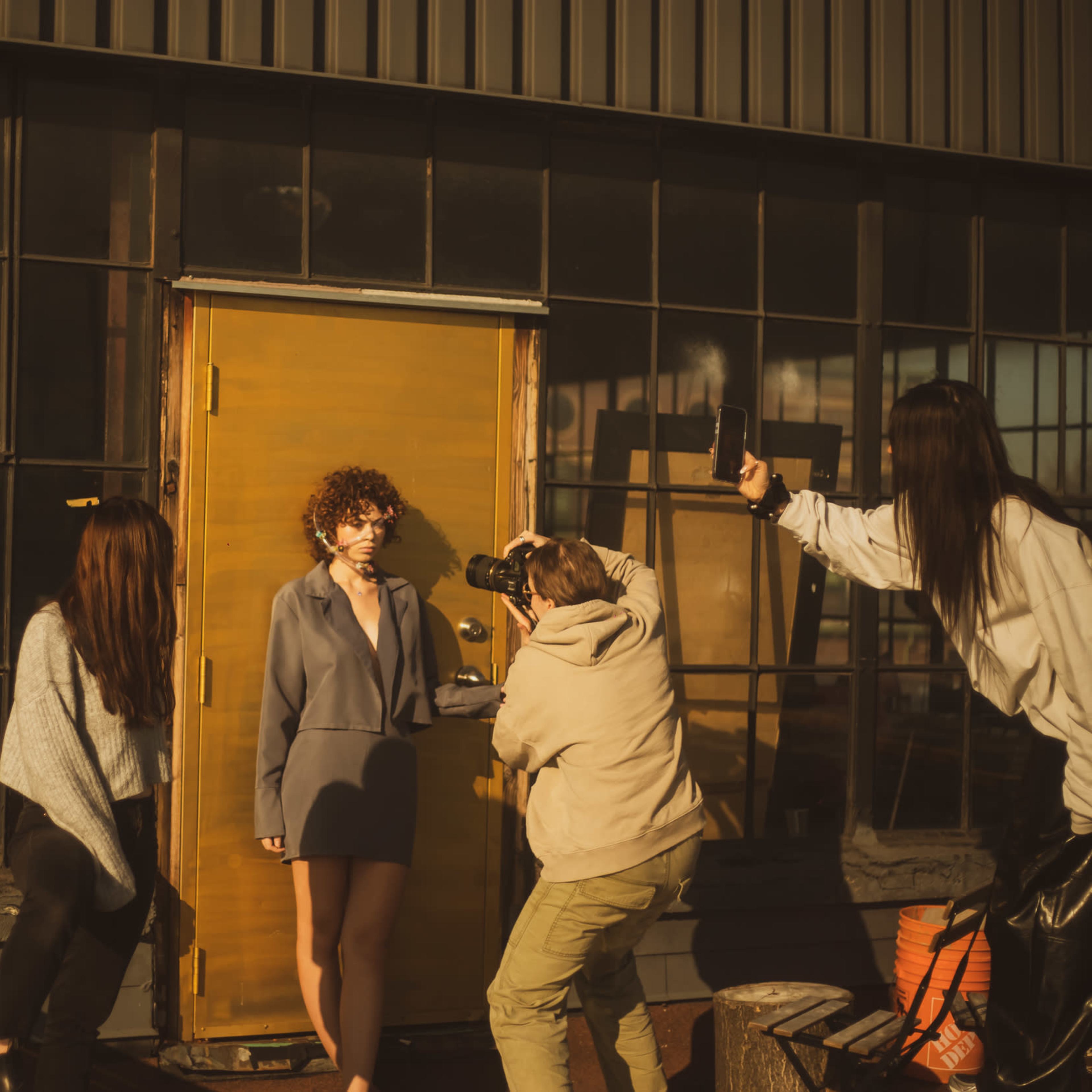 A model poses in front of a wooden door while a photographer captures her and two others observe.