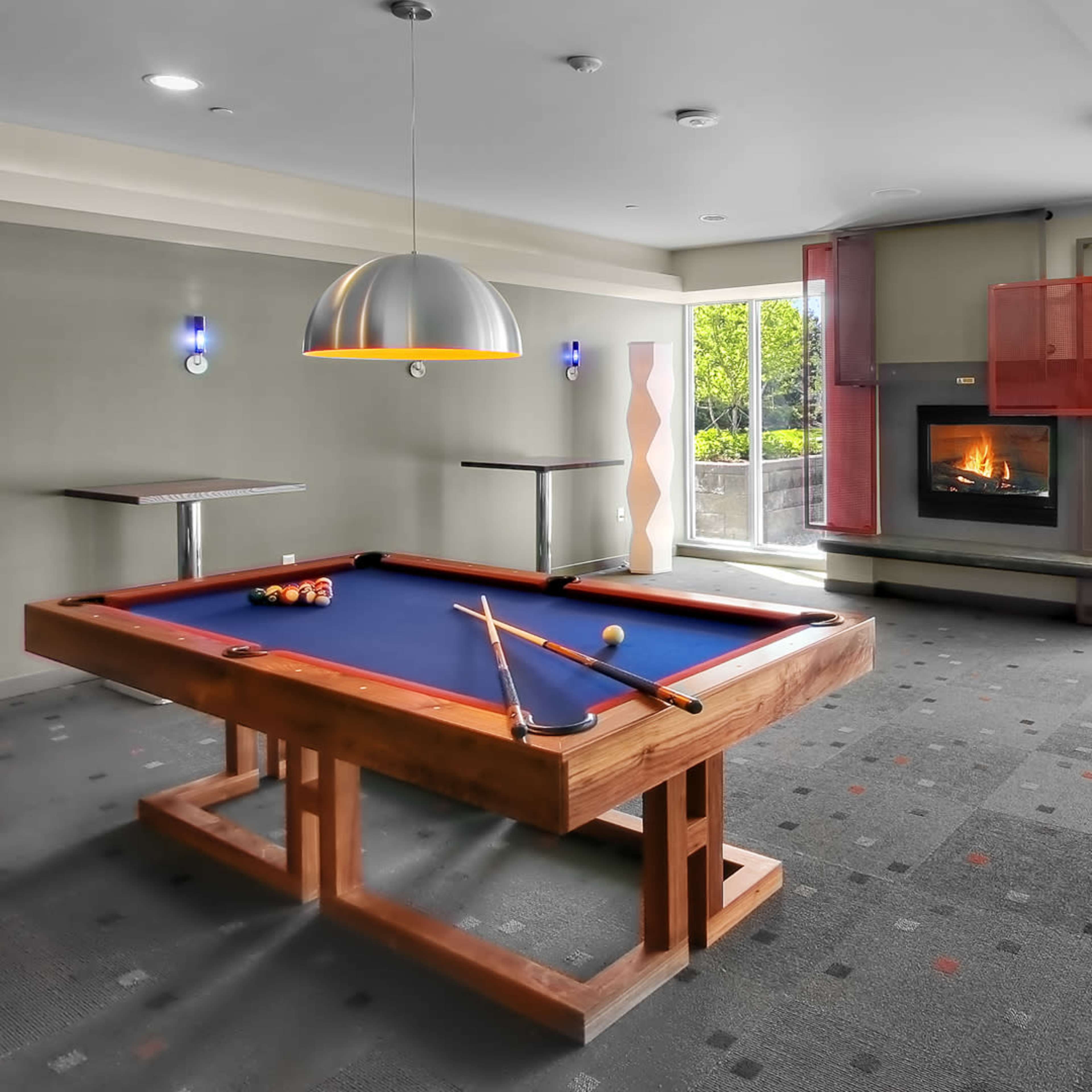 A billiards table in a recreational room with a fireplace and large windows overlooking an outdoor area.