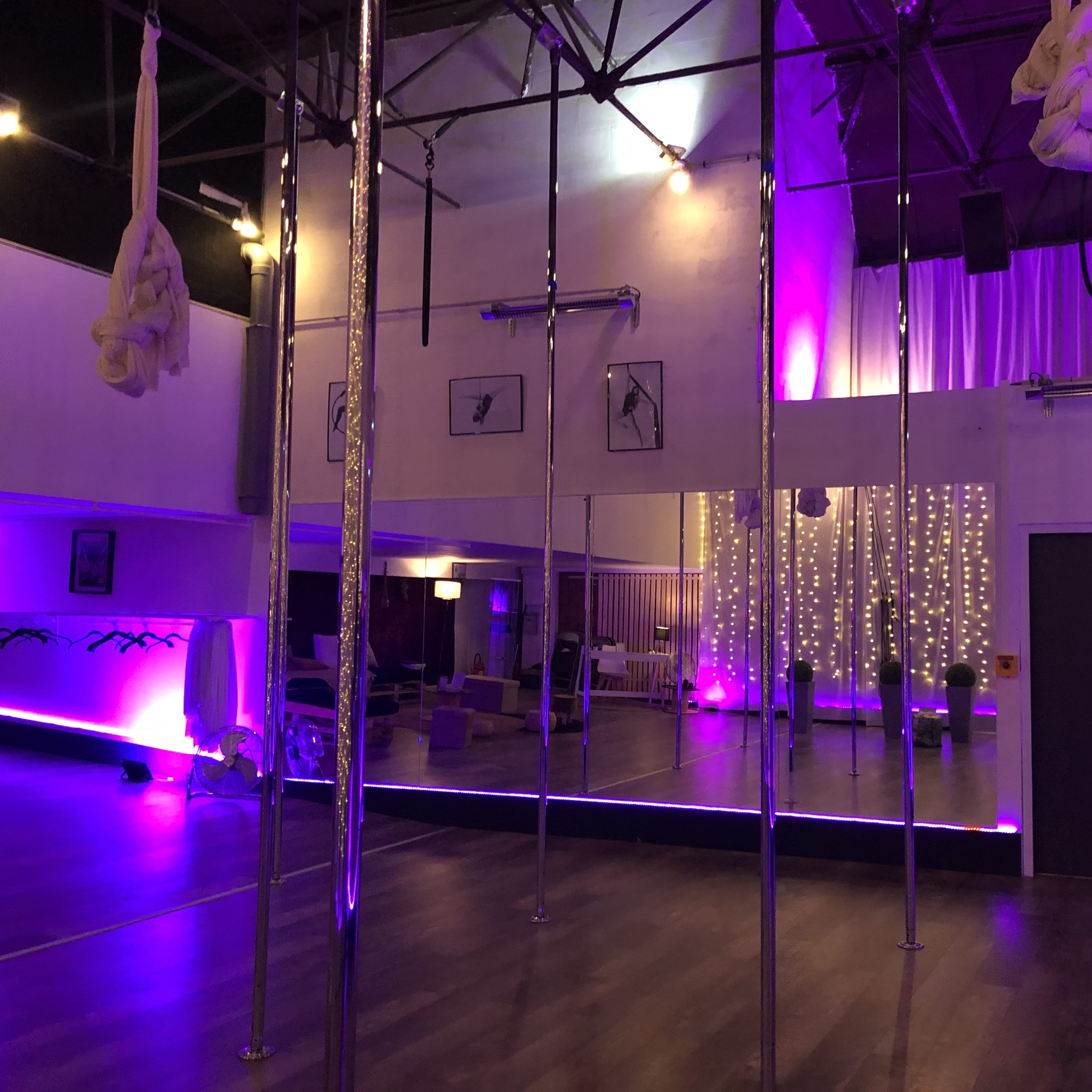 A spacious studio with several pole fixtures, mirrors, and ambient lighting, featuring purple hues and a sparkling backdrop.