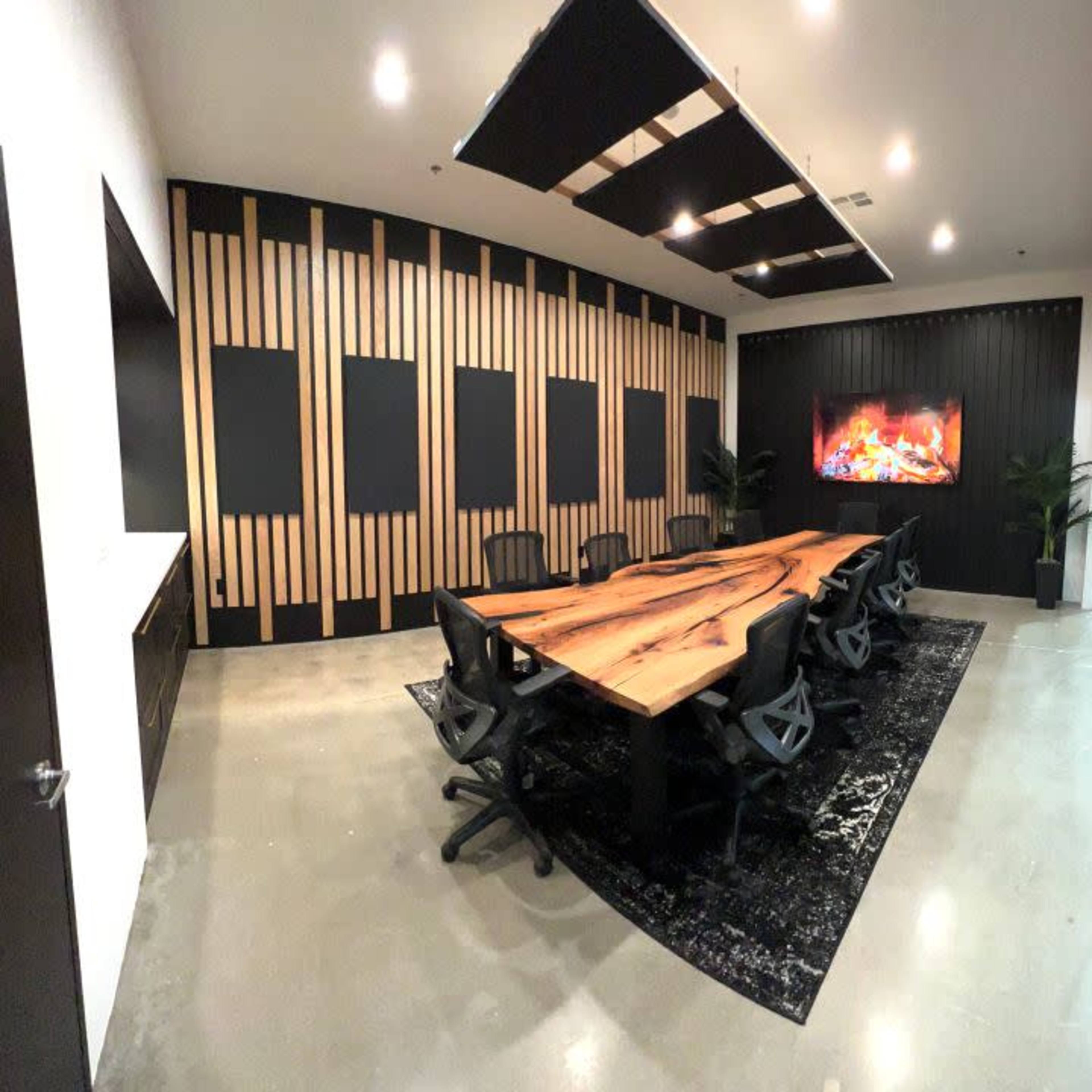 A modern conference room features a large wooden table surrounded by black chairs, with a textured wall and a digital fireplace display.