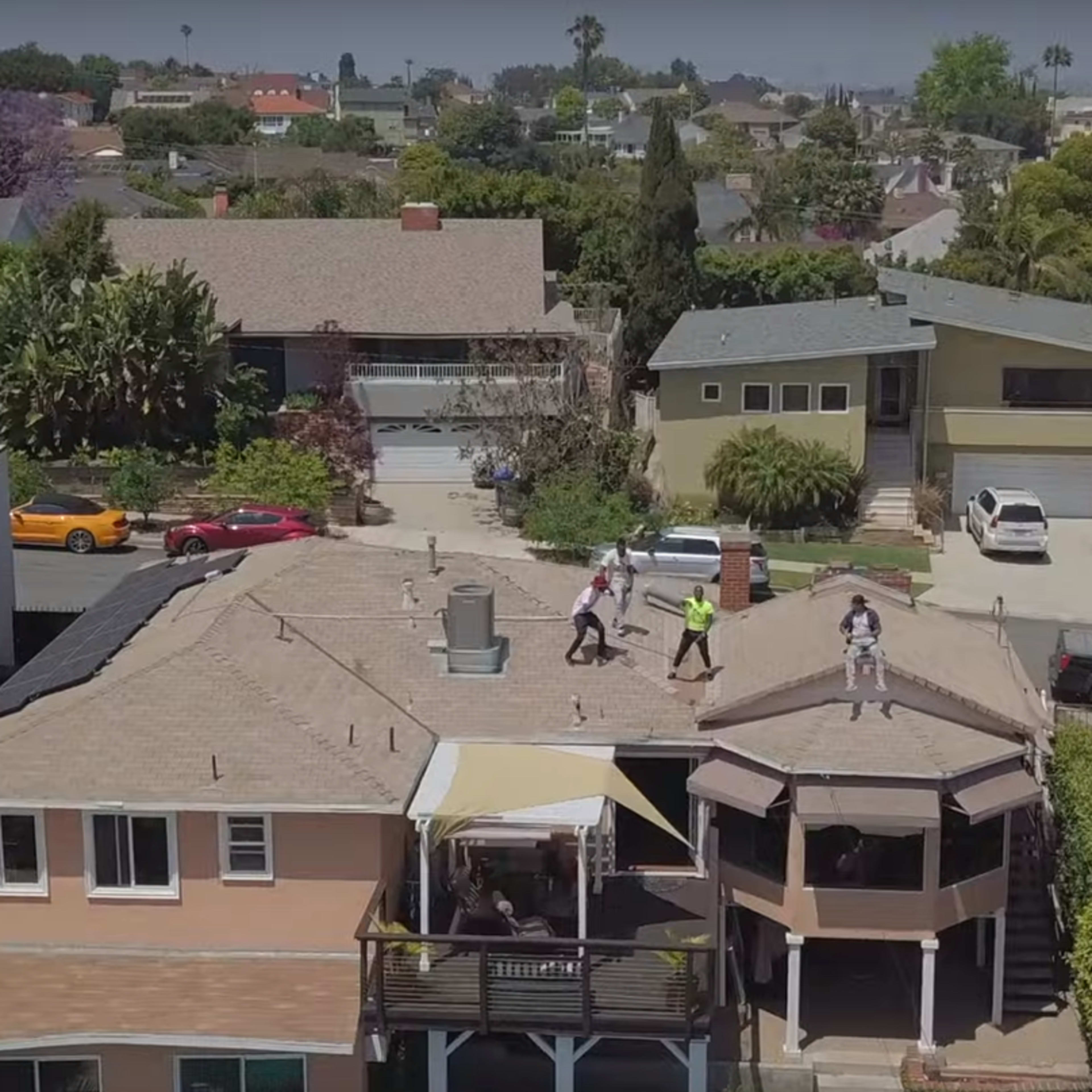 A group of workers is repairing the roof on a house in a suburban neighborhood surrounded by other residential properties.