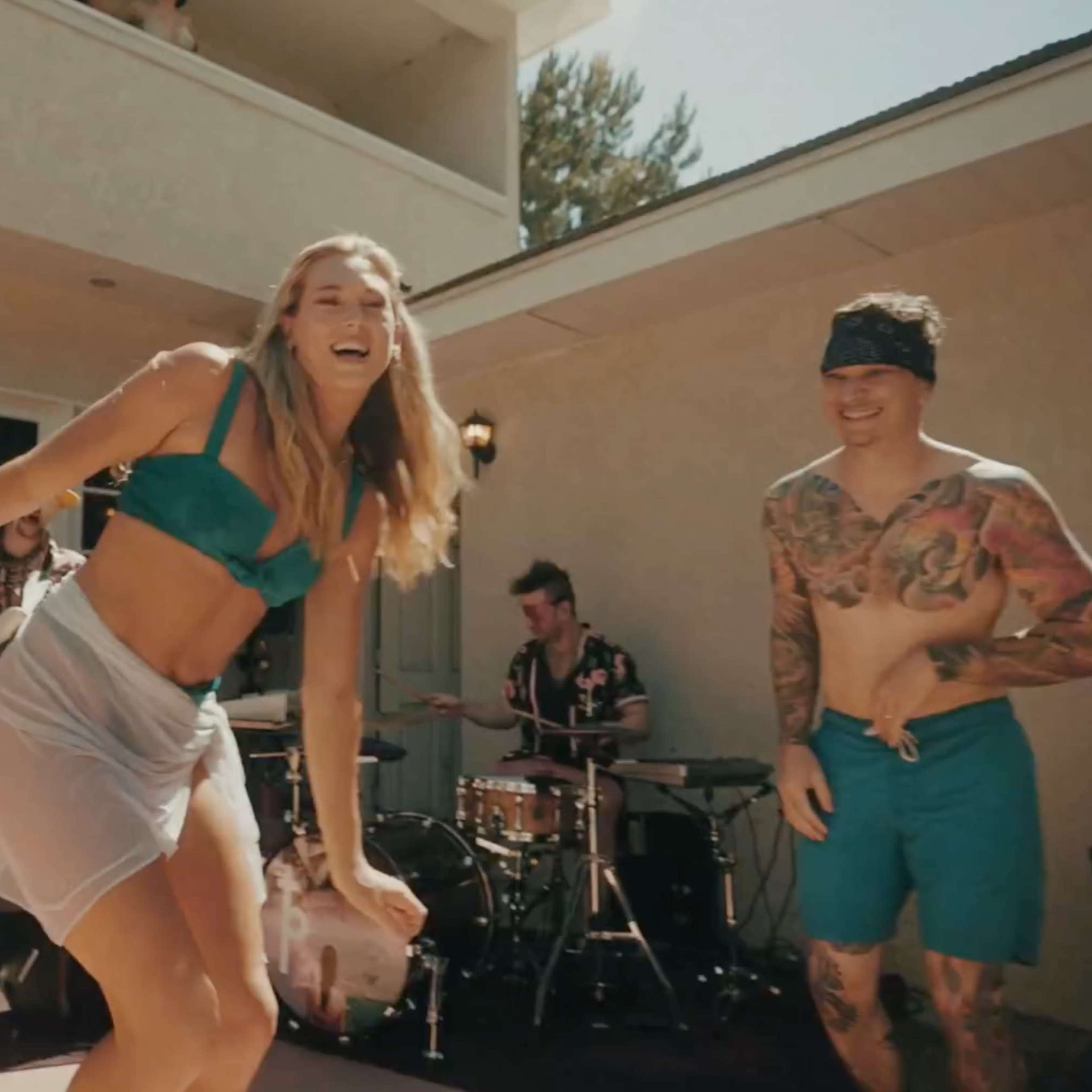 A group of people is dancing and enjoying music outdoors near a house with a band playing in the background.