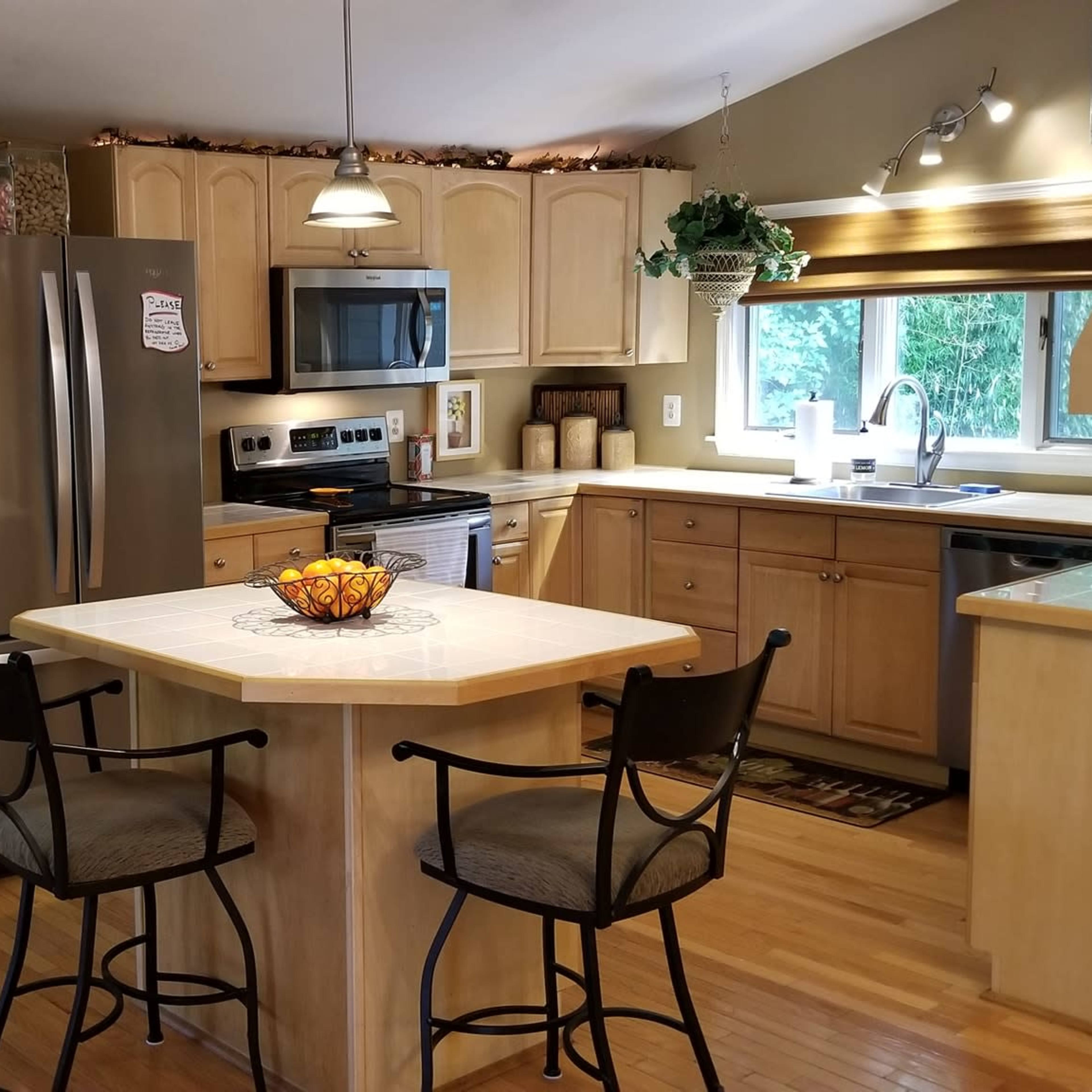 A well-lit kitchen with wooden cabinetry, stainless steel appliances, and a central island with bar stools.