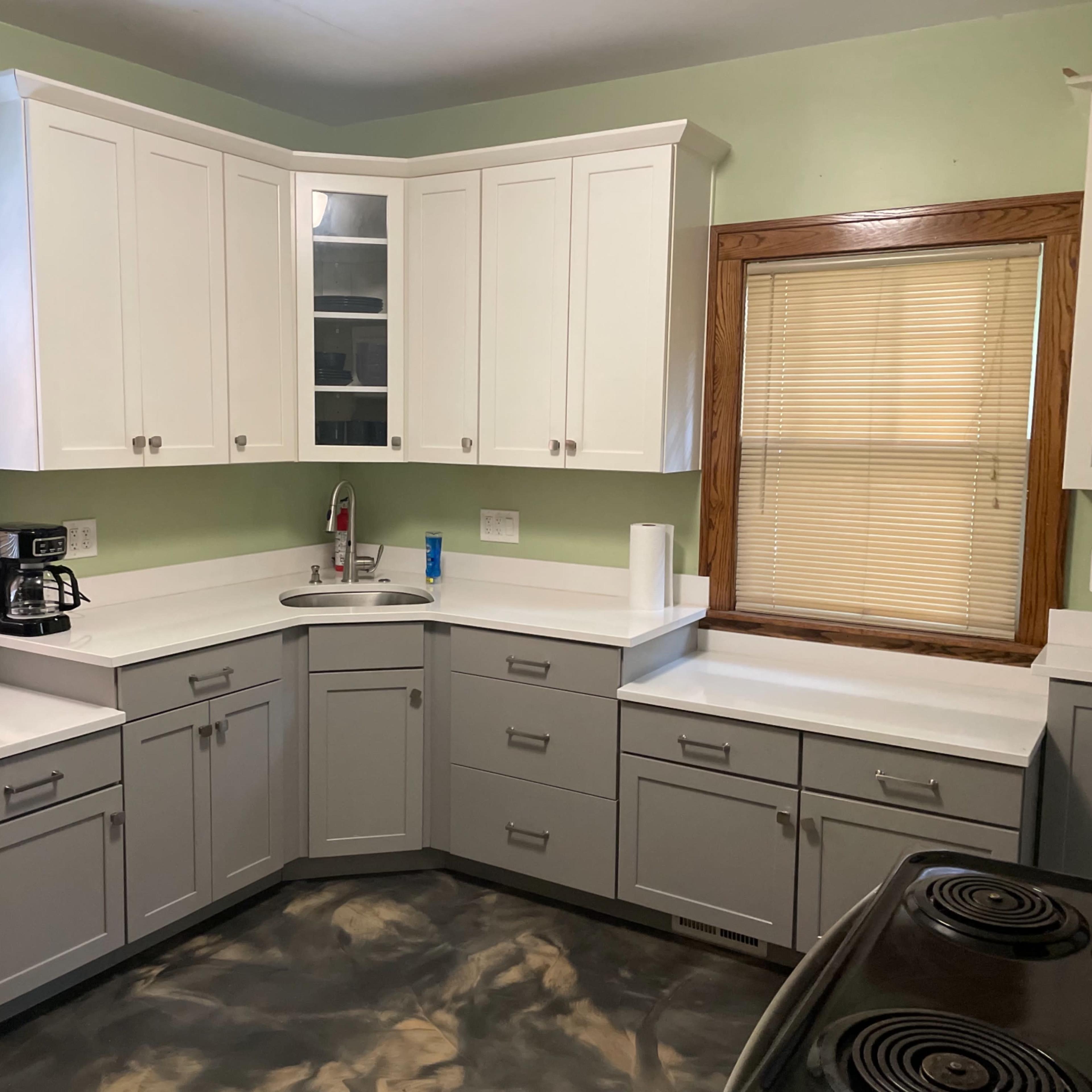 A kitchen features gray cabinets, a stainless steel refrigerator, and a stove, with a sink on the counter beneath a window.