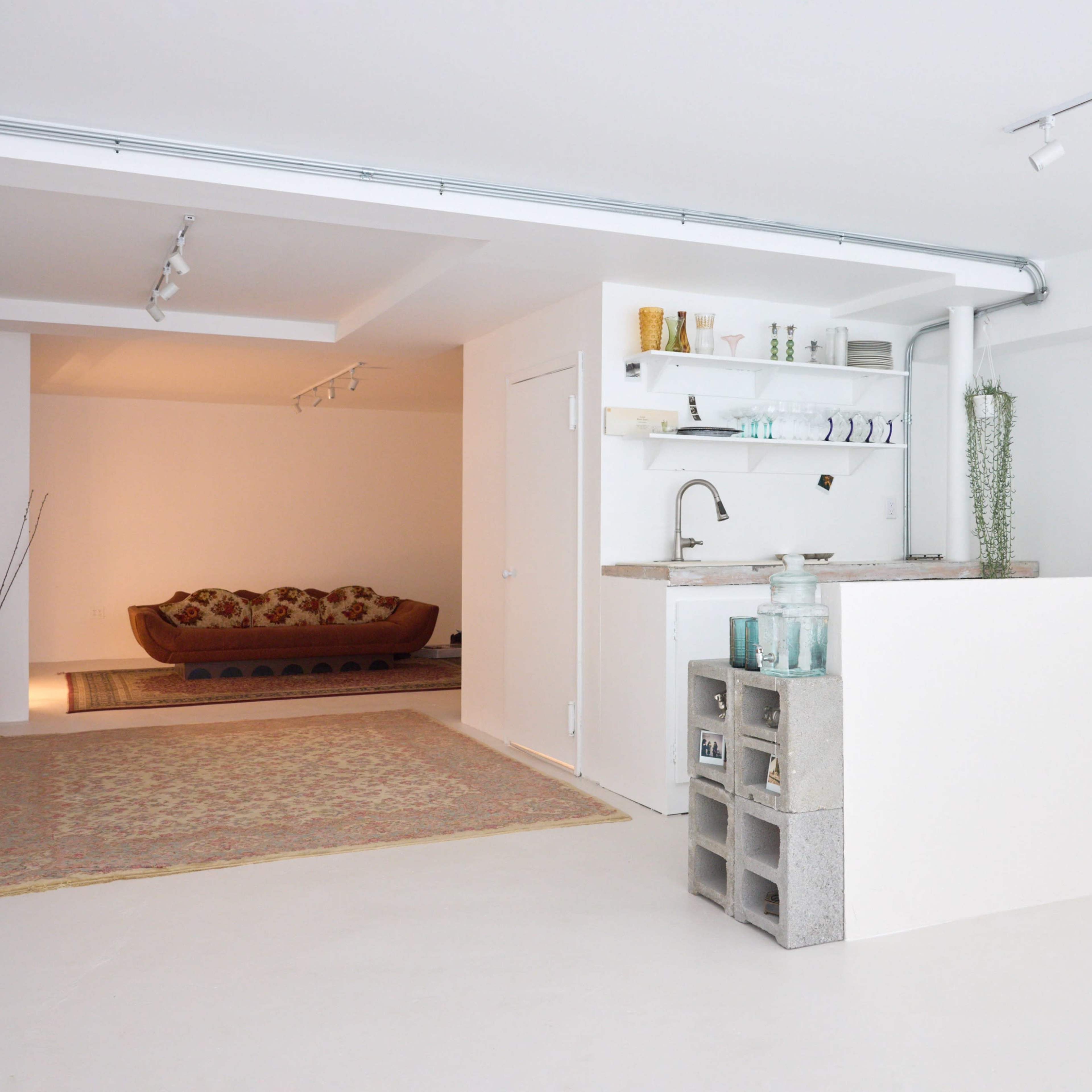 A spacious, modern interior with a bar-like counter made of concrete blocks, leading to a living area with a patterned rug and a sofa.