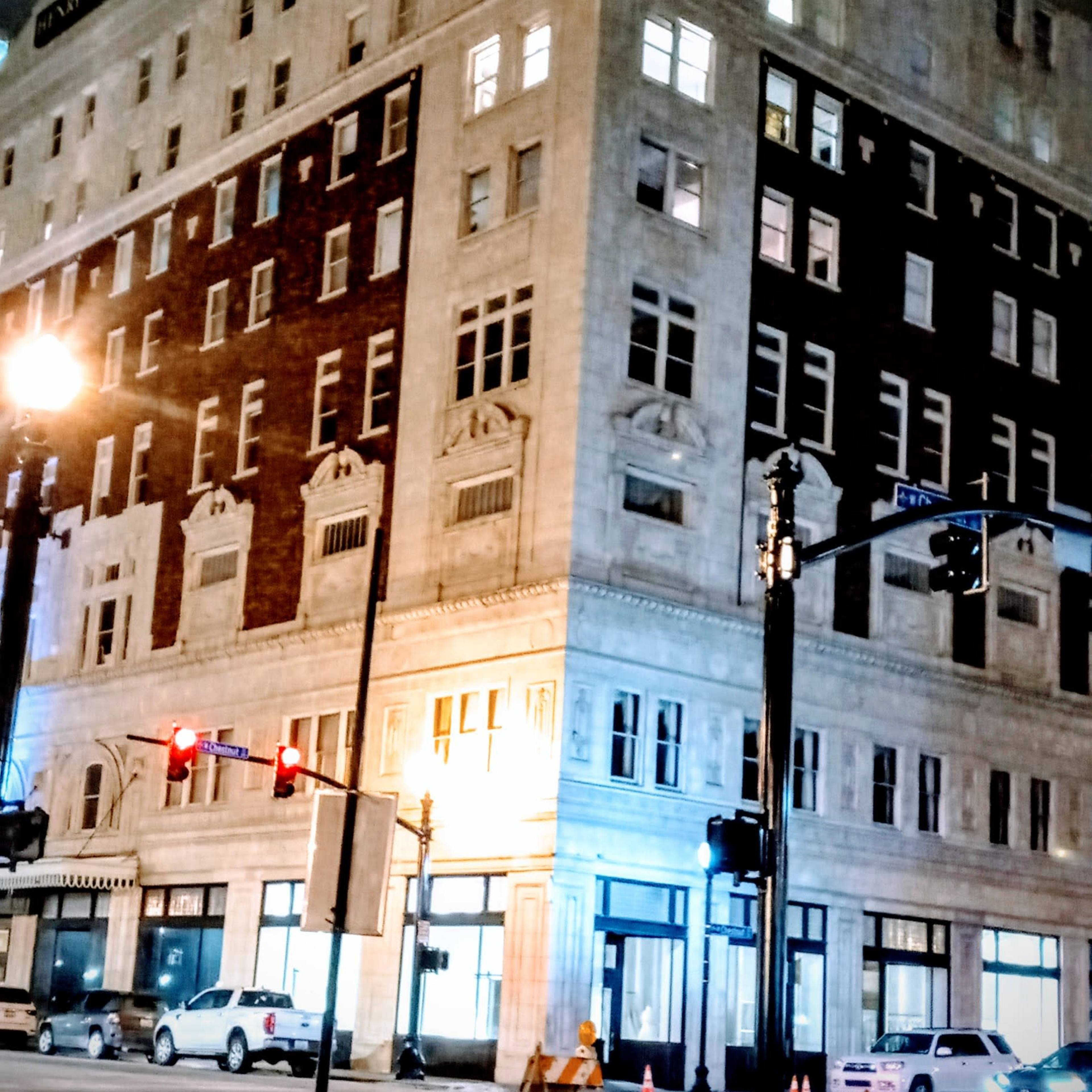 A historic multi-story building with a mix of light and dark facade is illuminated at night, featuring few visible windows lit and street lights nearby.