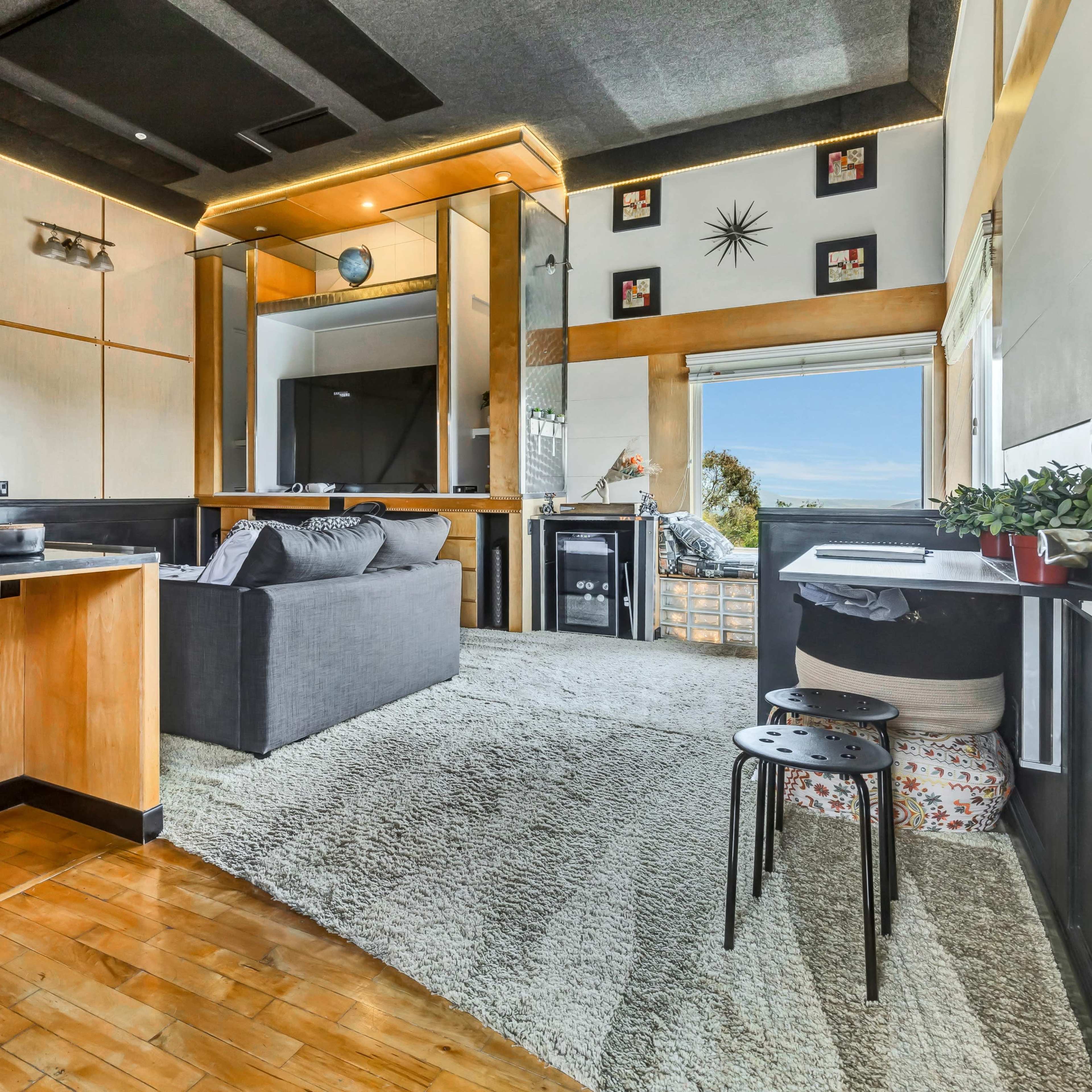 A modern living area with a gray sofa, wooden accents, and large windows offering a view.