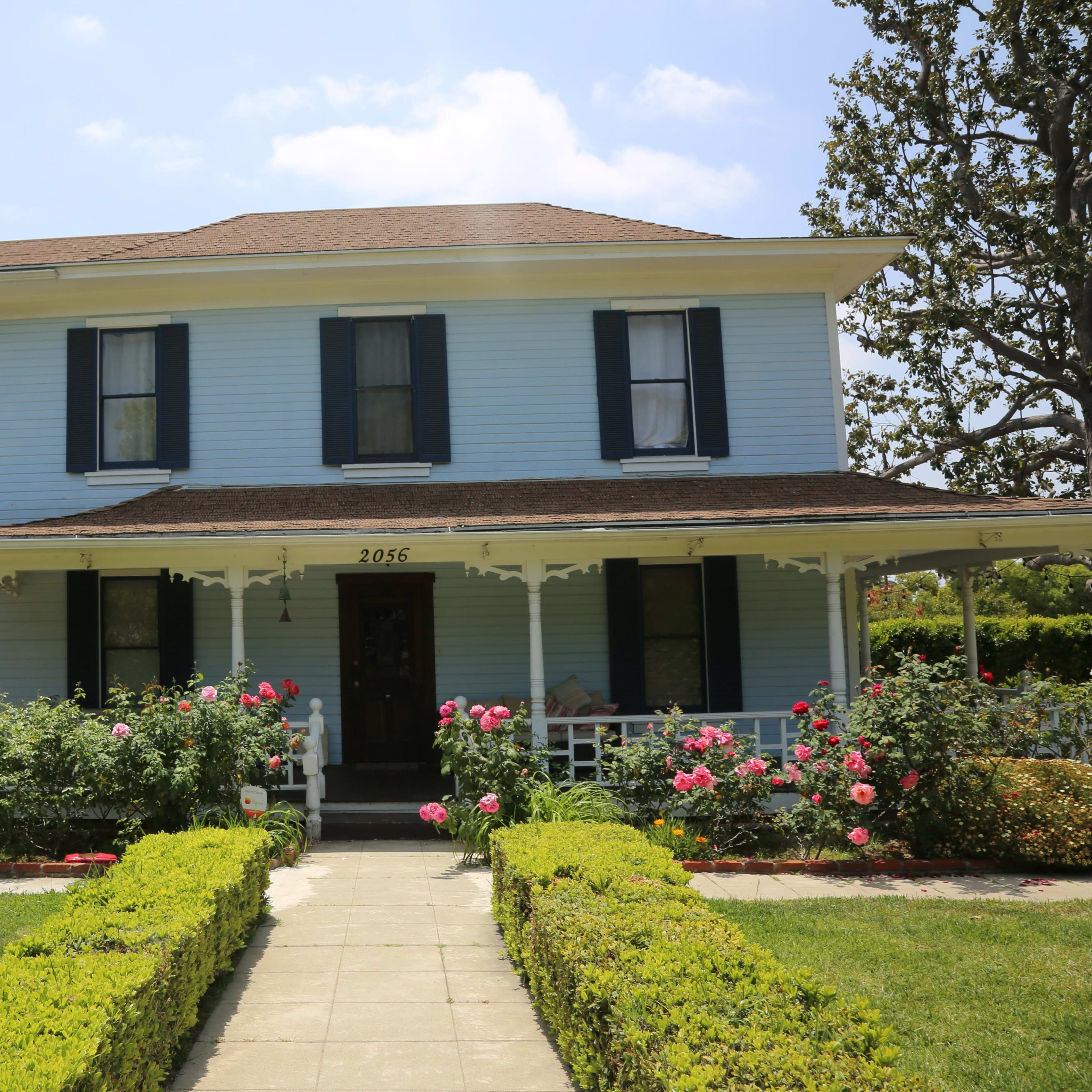 A light blue two-story house with black shutters surrounded by flower beds and a well-maintained lawn.