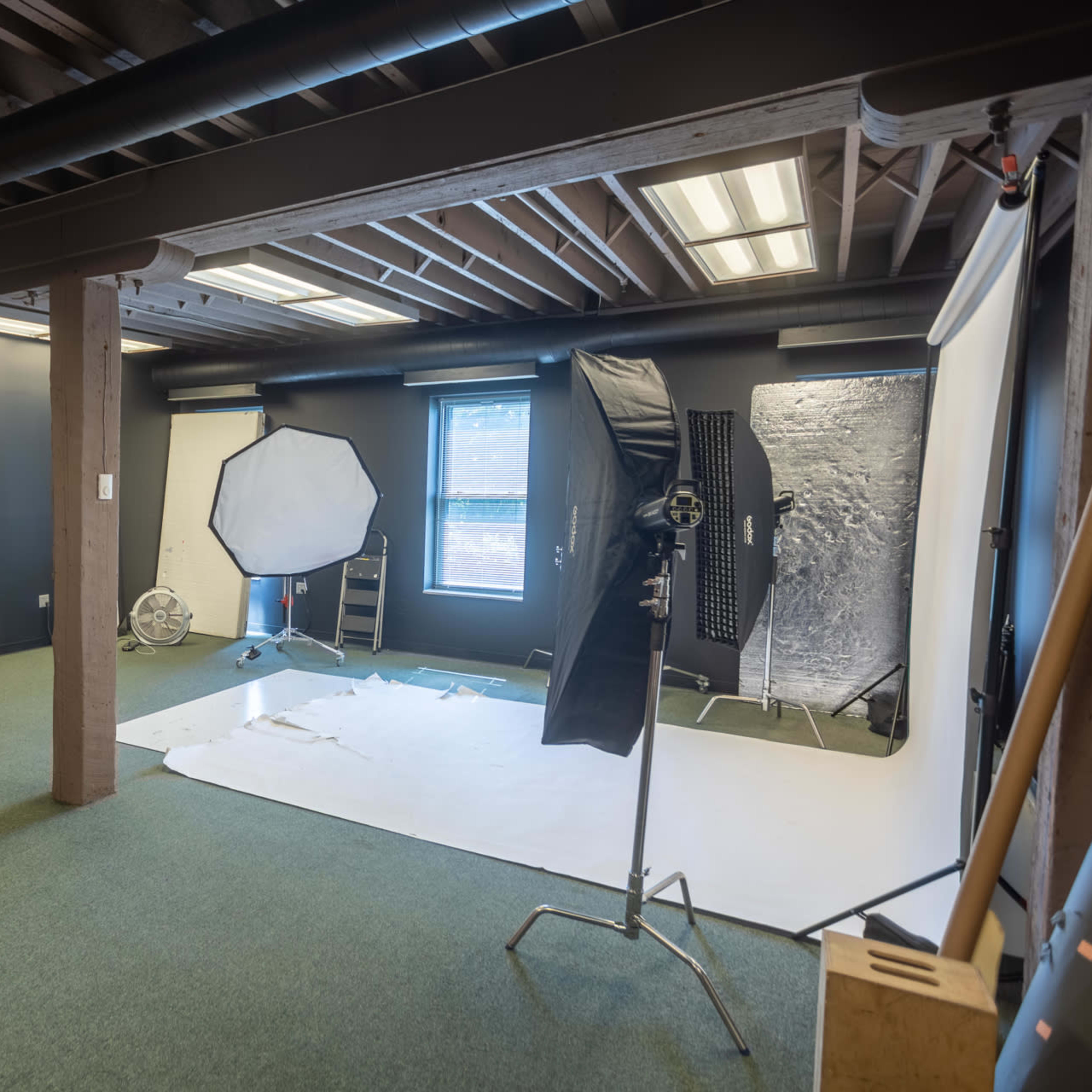 A photography studio with a partially set-up backdrop, a large softbox, and various lighting equipment arranged in a spacious room.