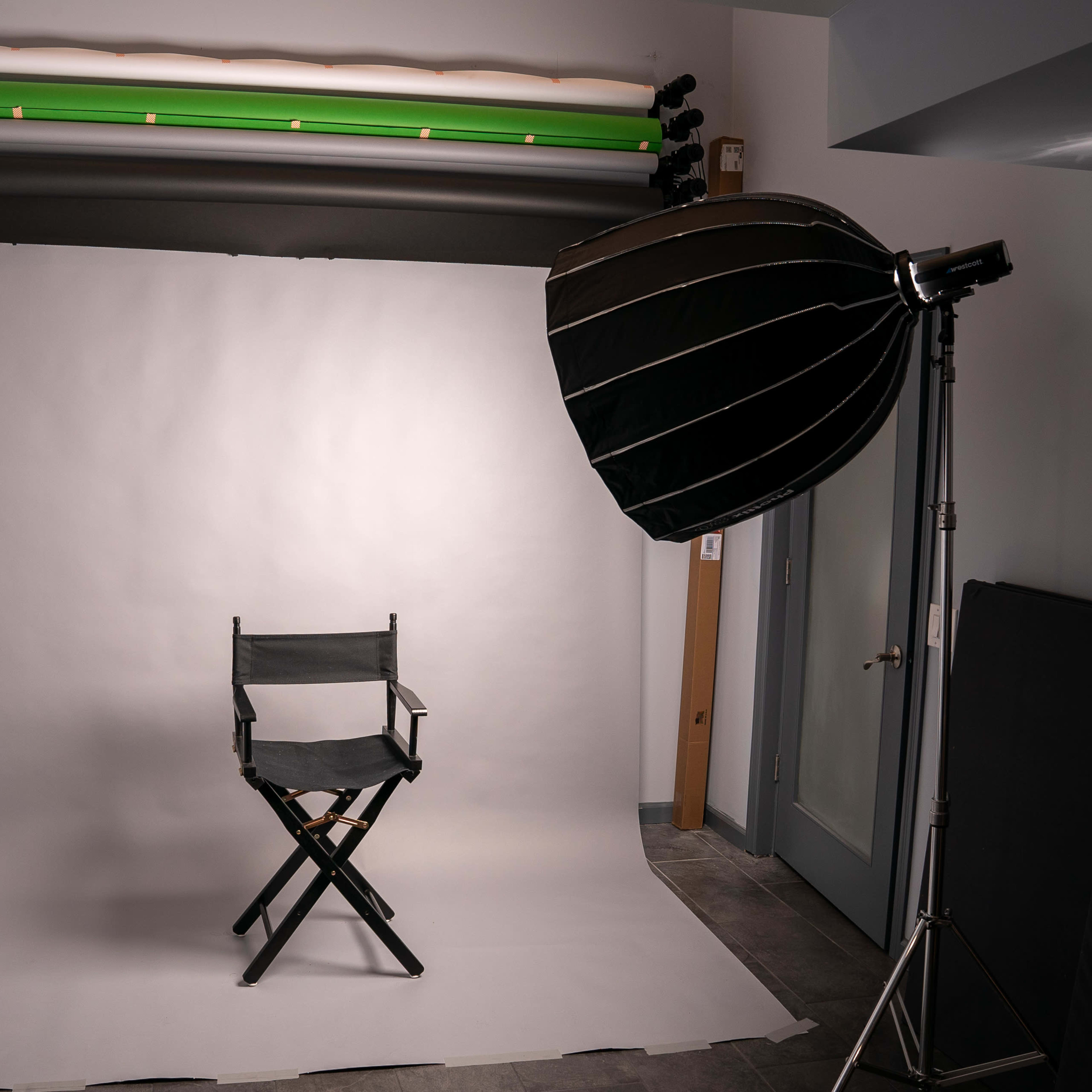 A photography studio with a folding chair positioned on a light backdrop, complemented by studio lighting equipment on the side.