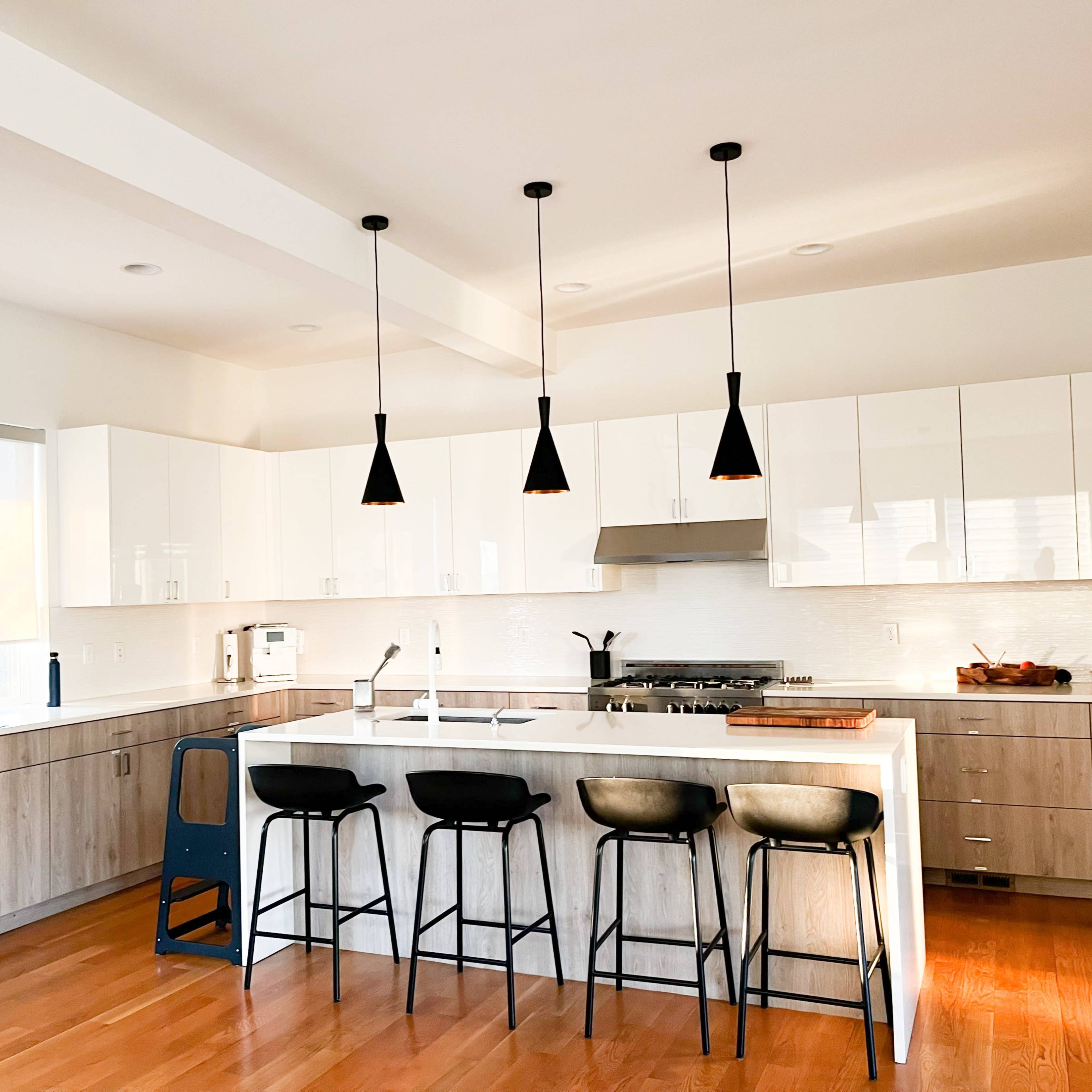 A modern kitchen features a large island with bar stools, stainless steel appliances, and pendant lighting over the countertop.
