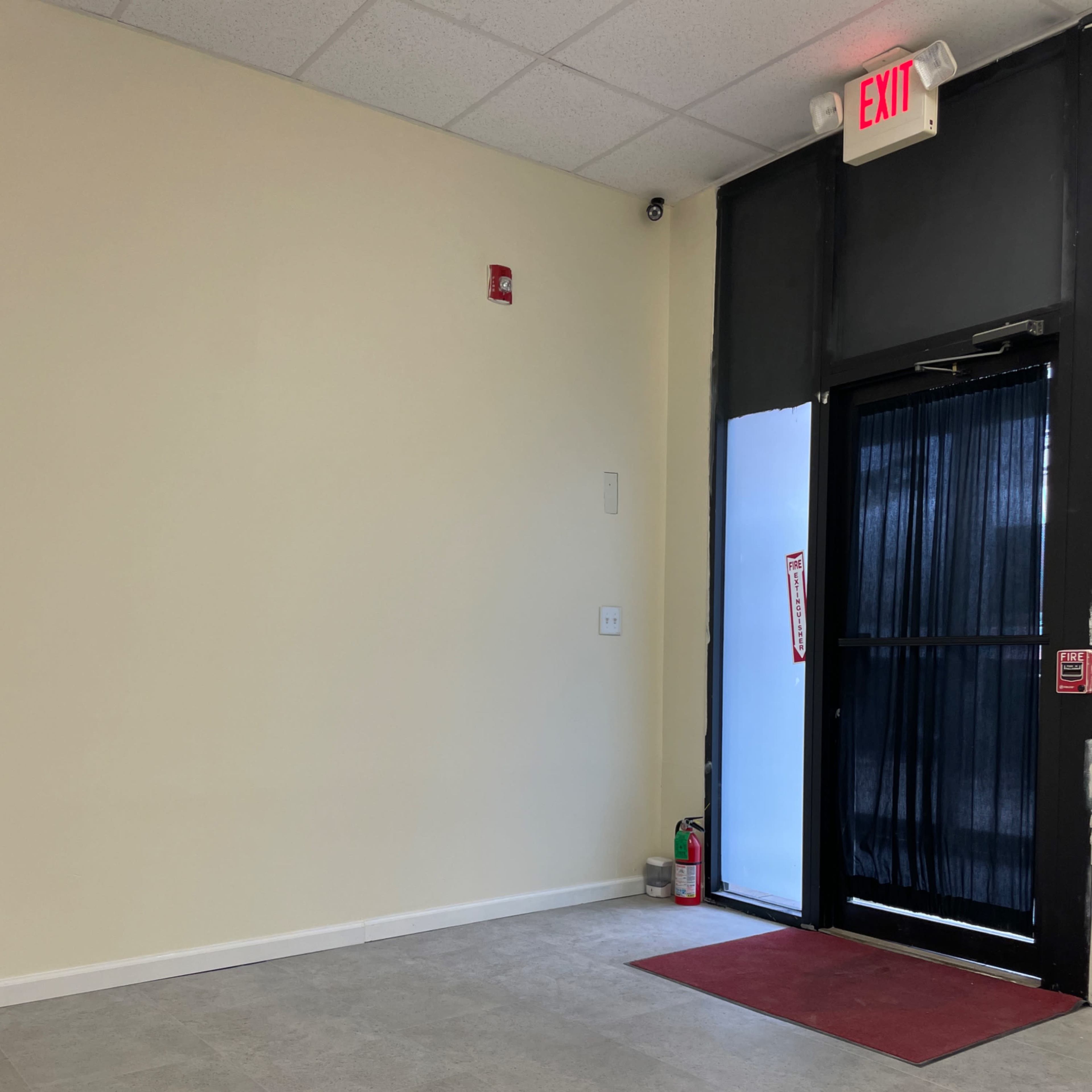 An empty room with a tiled floor, a door that opens to the outside, and an exit sign above the door.