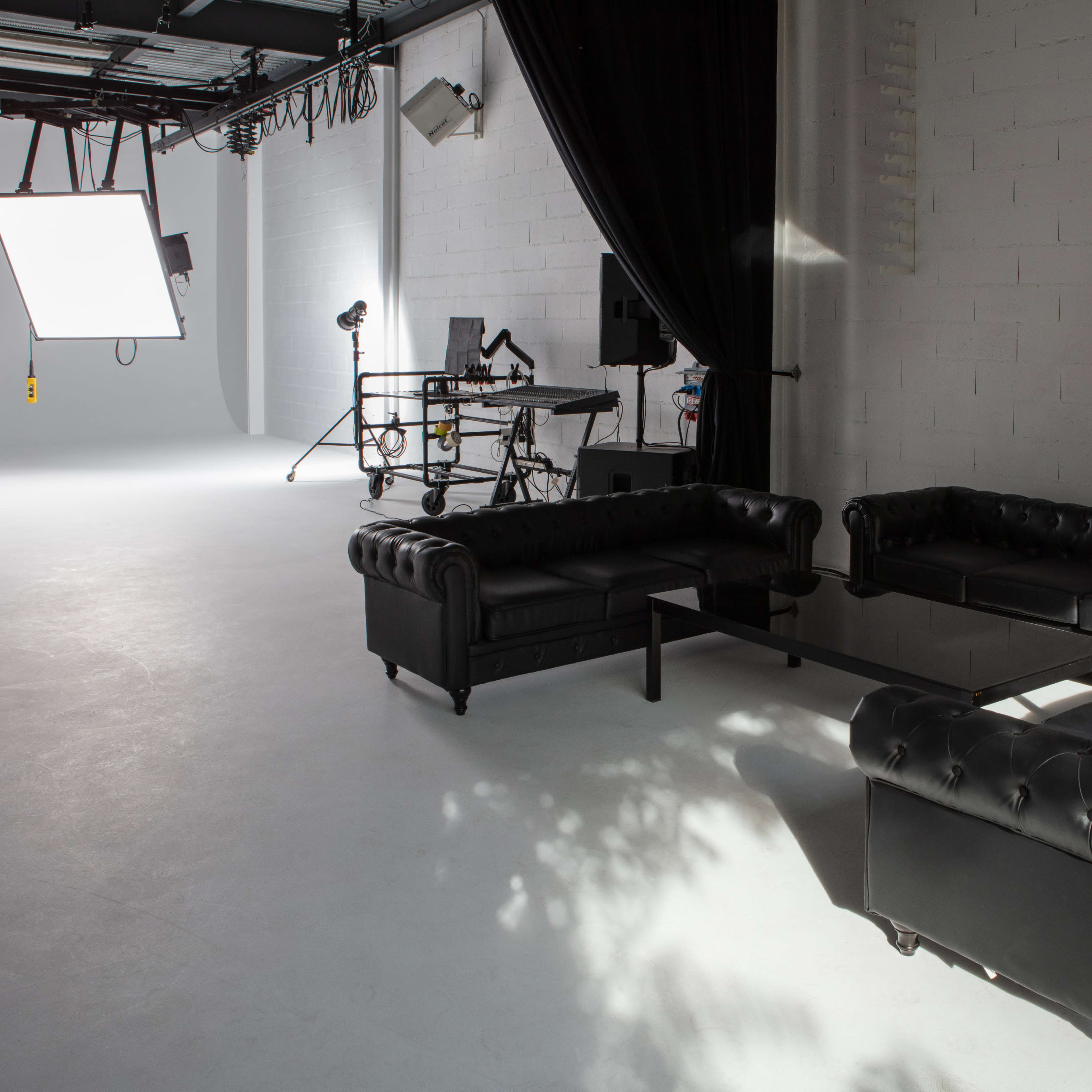 A photography studio with black leather couches arranged around a glass table and lighting equipment in the background.
