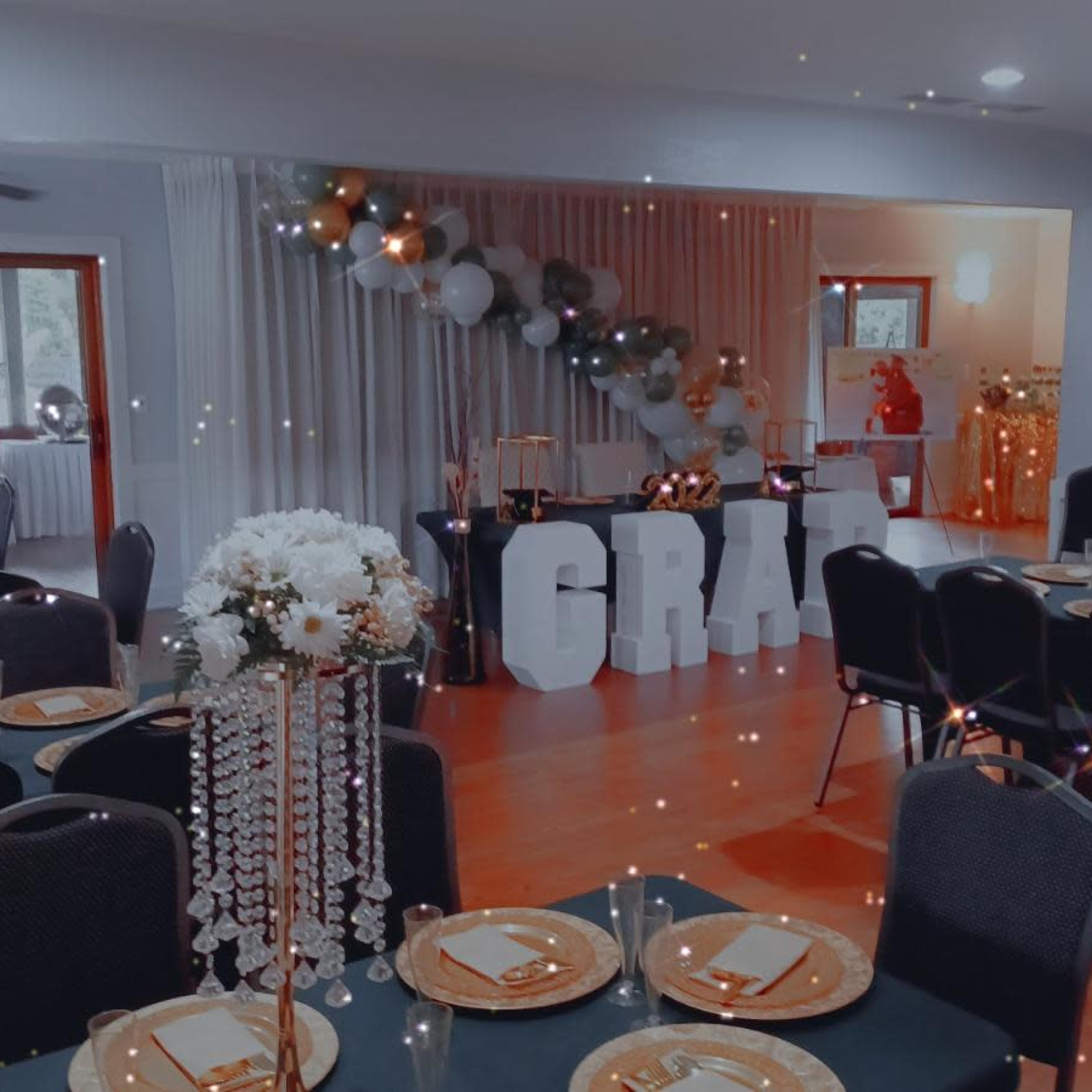 A banquet hall set up for a celebration, featuring tables with black cloths, centerpieces, and large decorative letters that spell "GRAD."
