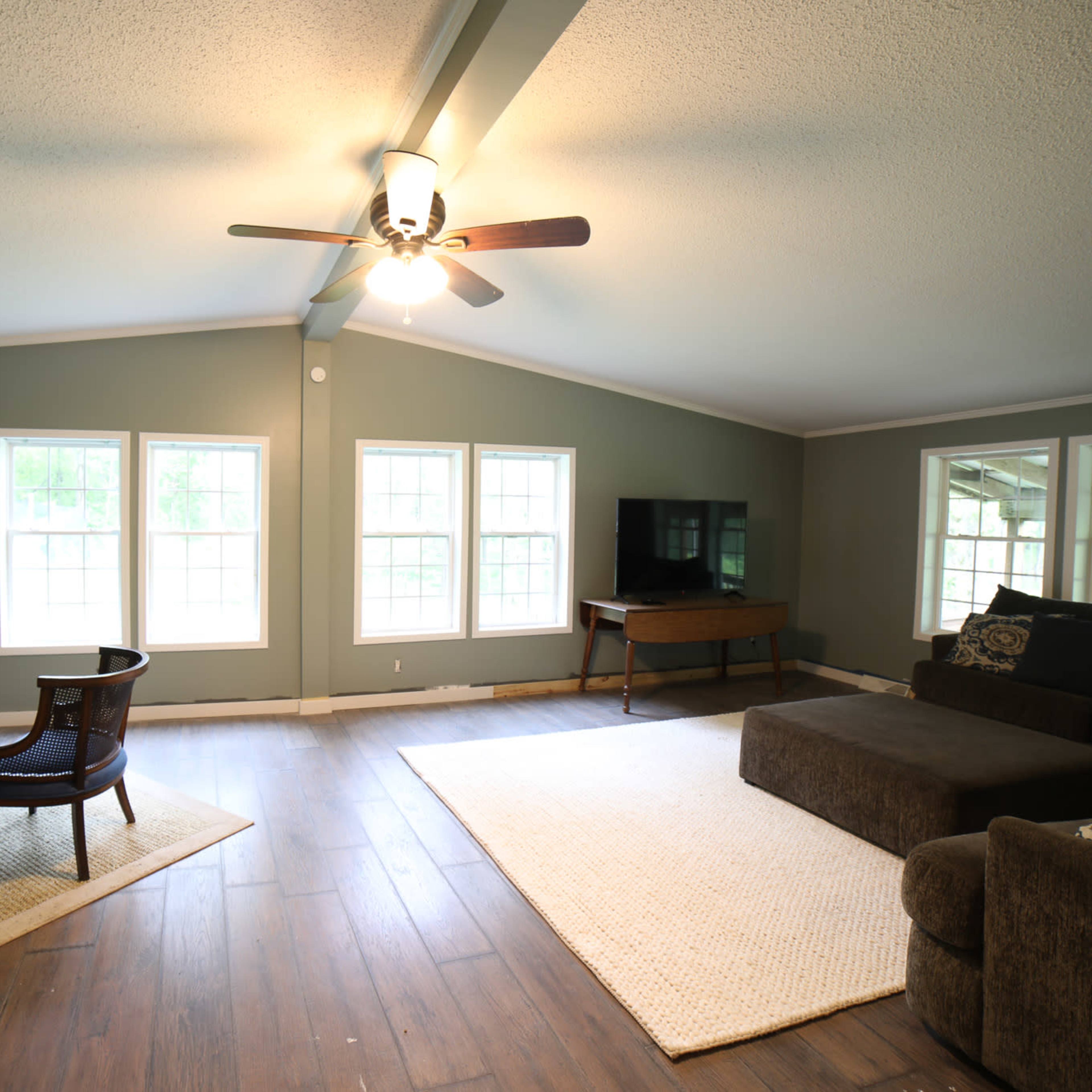 The living room features a fireplace, two chairs, a sectional sofa, and large windows that provide natural light.
