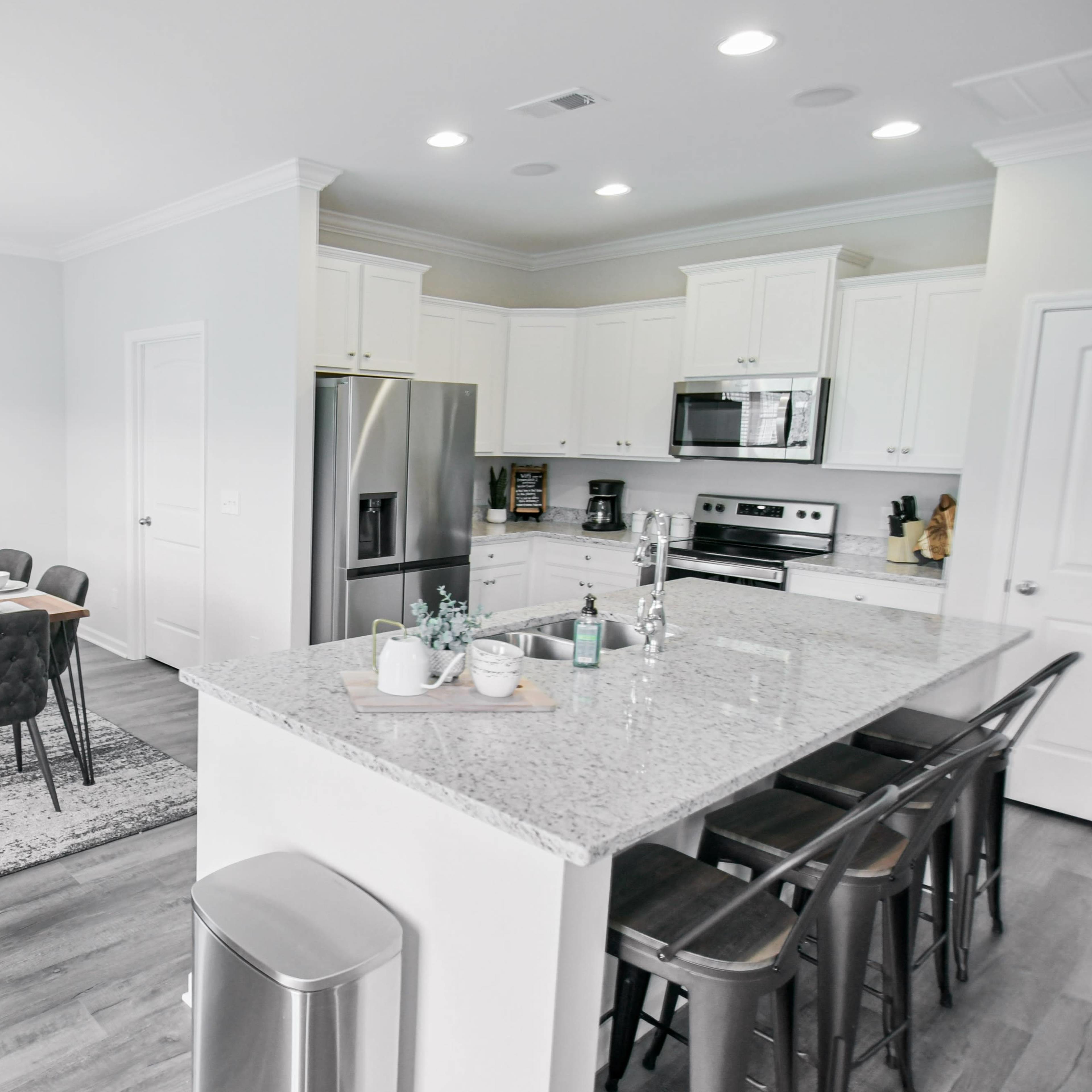 A modern kitchen with stainless steel appliances and granite countertops opens up to a dining area featuring a wooden table set for meals.