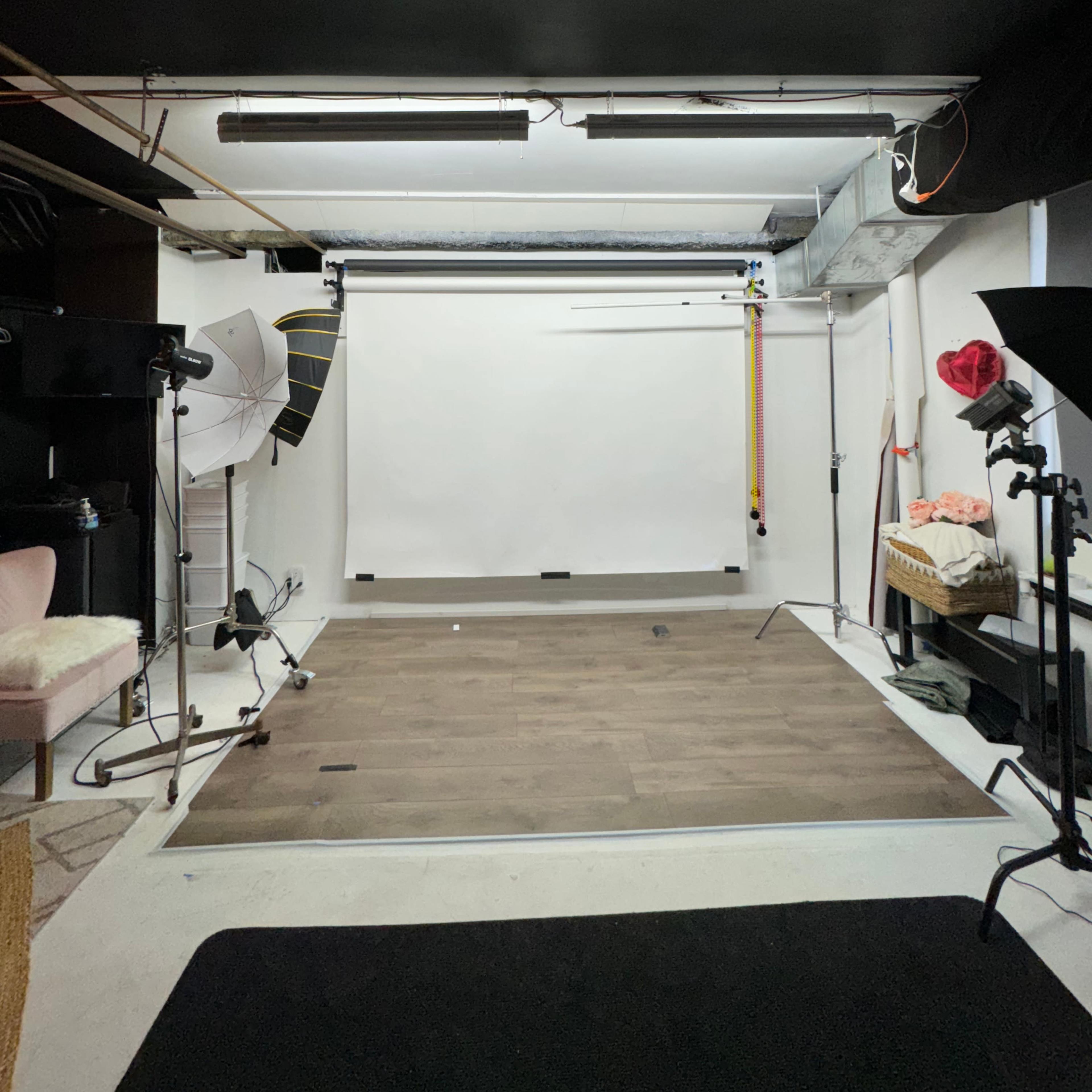 A dimly lit photography studio with a white backdrop and various lighting equipment positioned around the space.