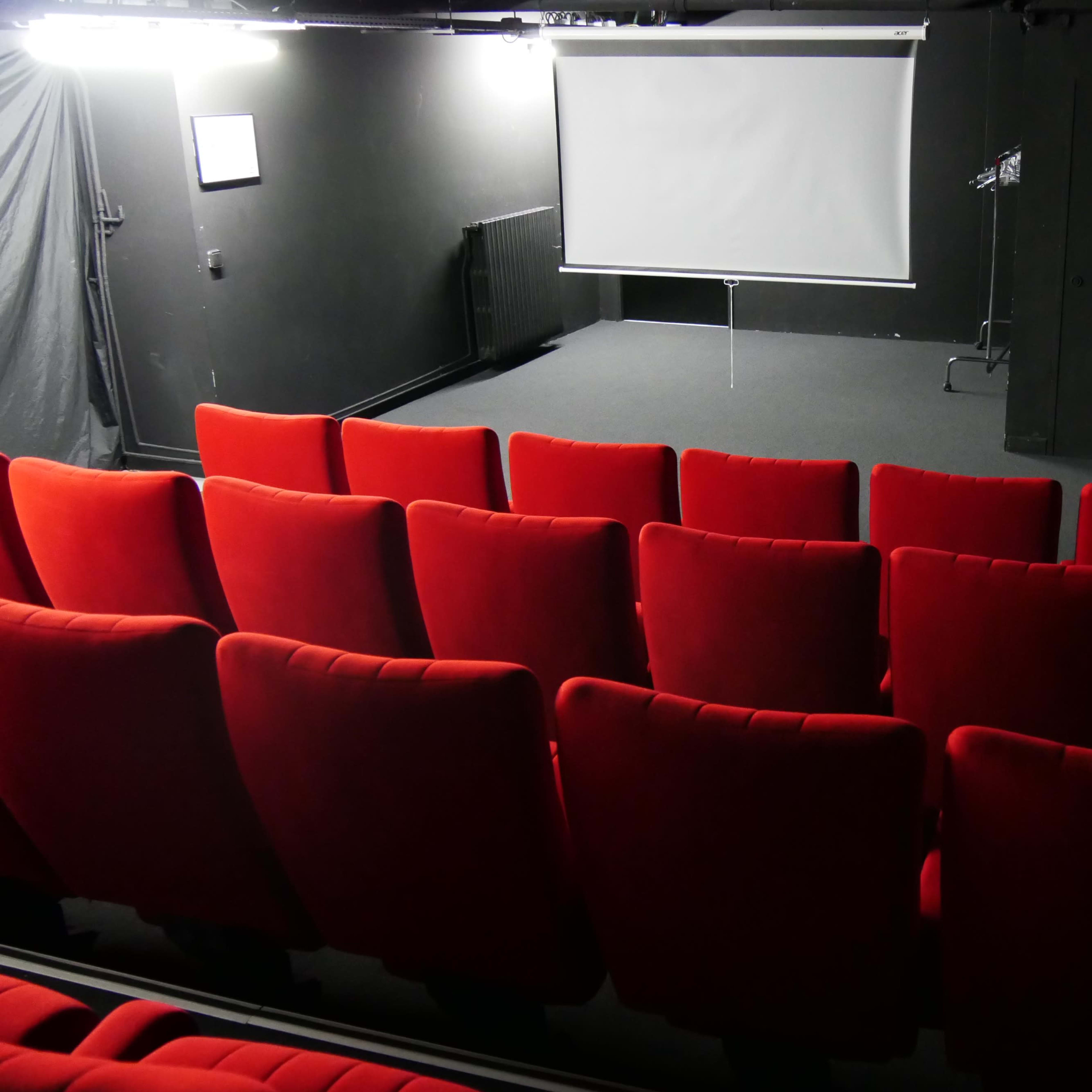A small theater space with red seating facing a blank projection screen.