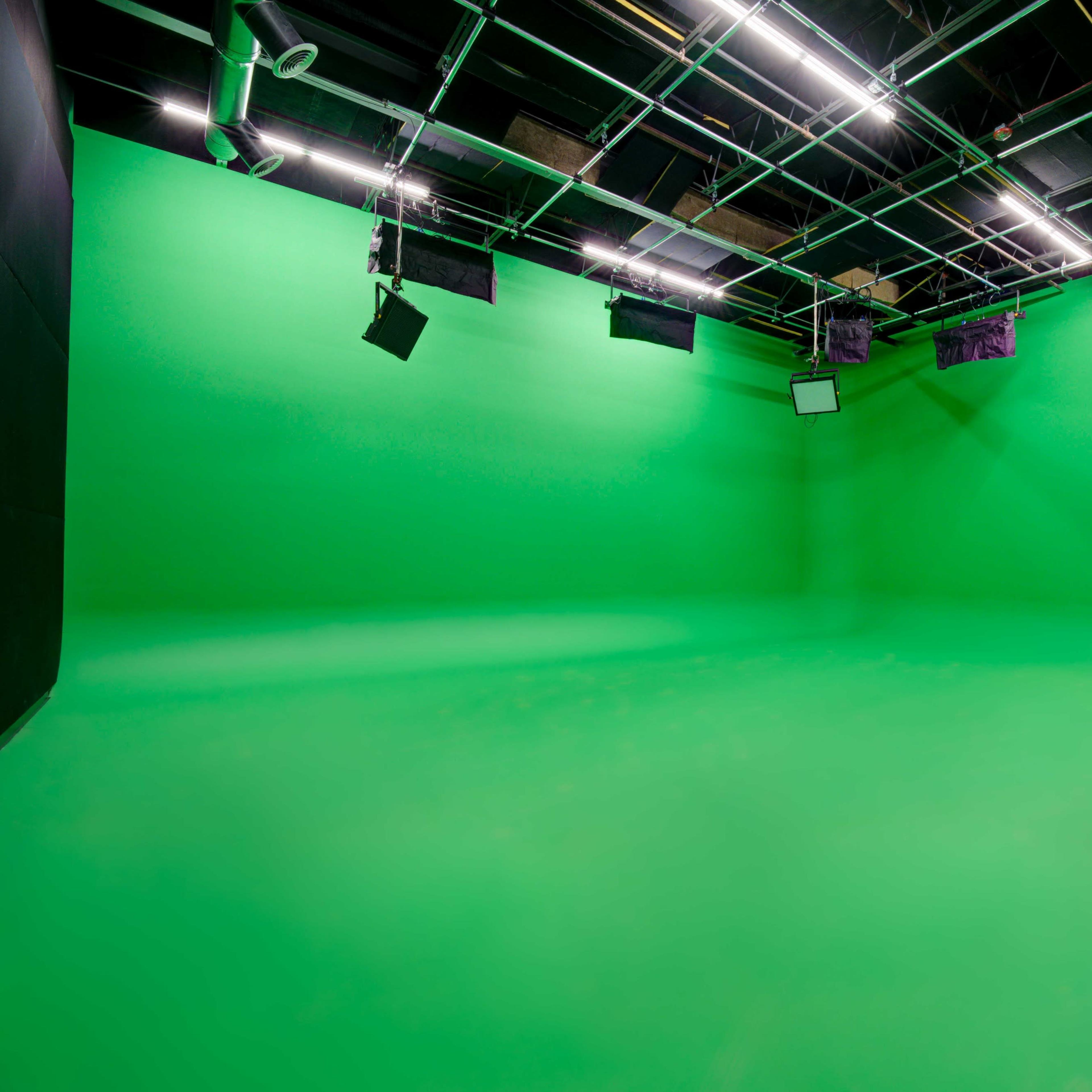 A large green screen studio with overhead lighting and dim walls.