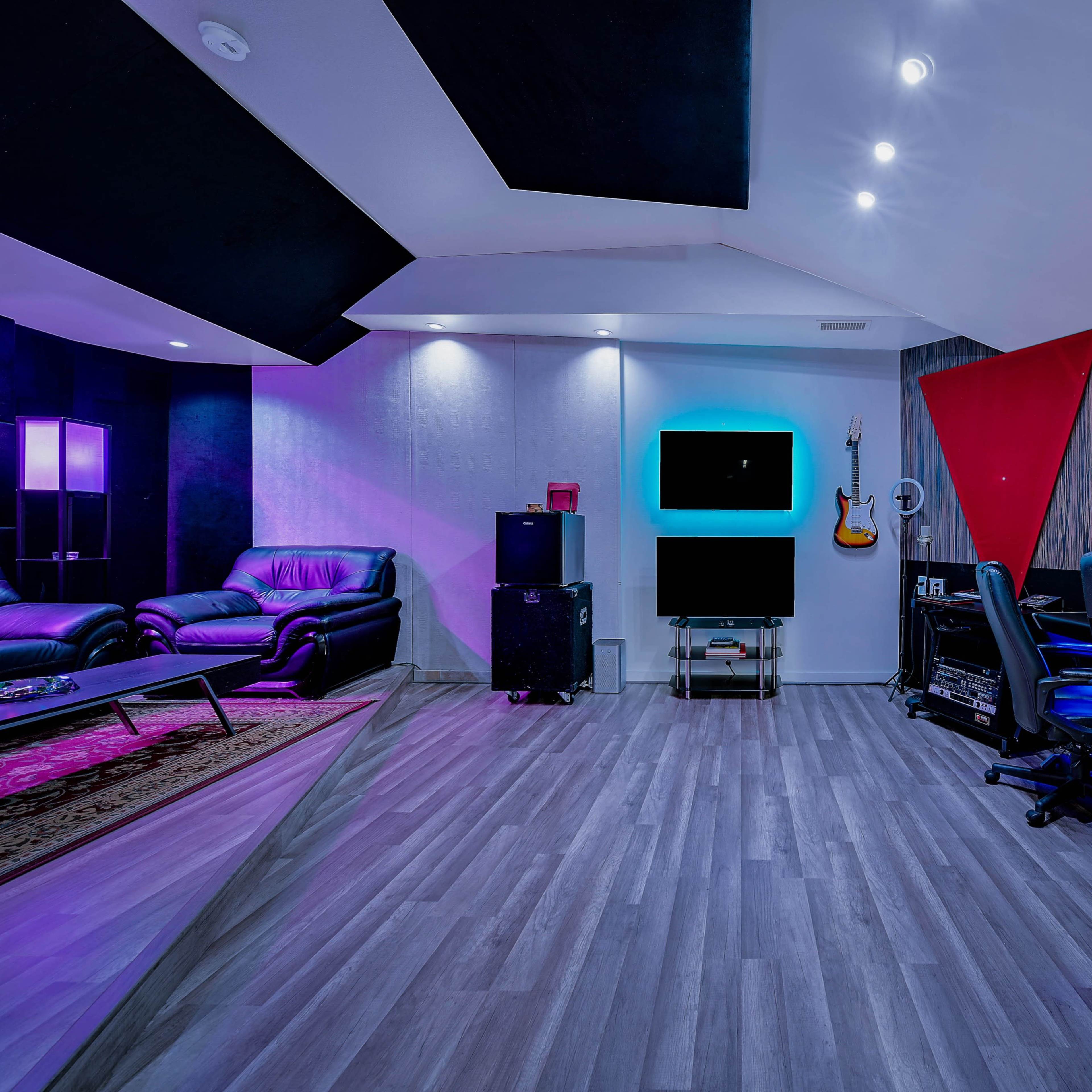 A modern recording studio featuring a comfortable seating area, a large mixing console, and colorful ambient lighting.