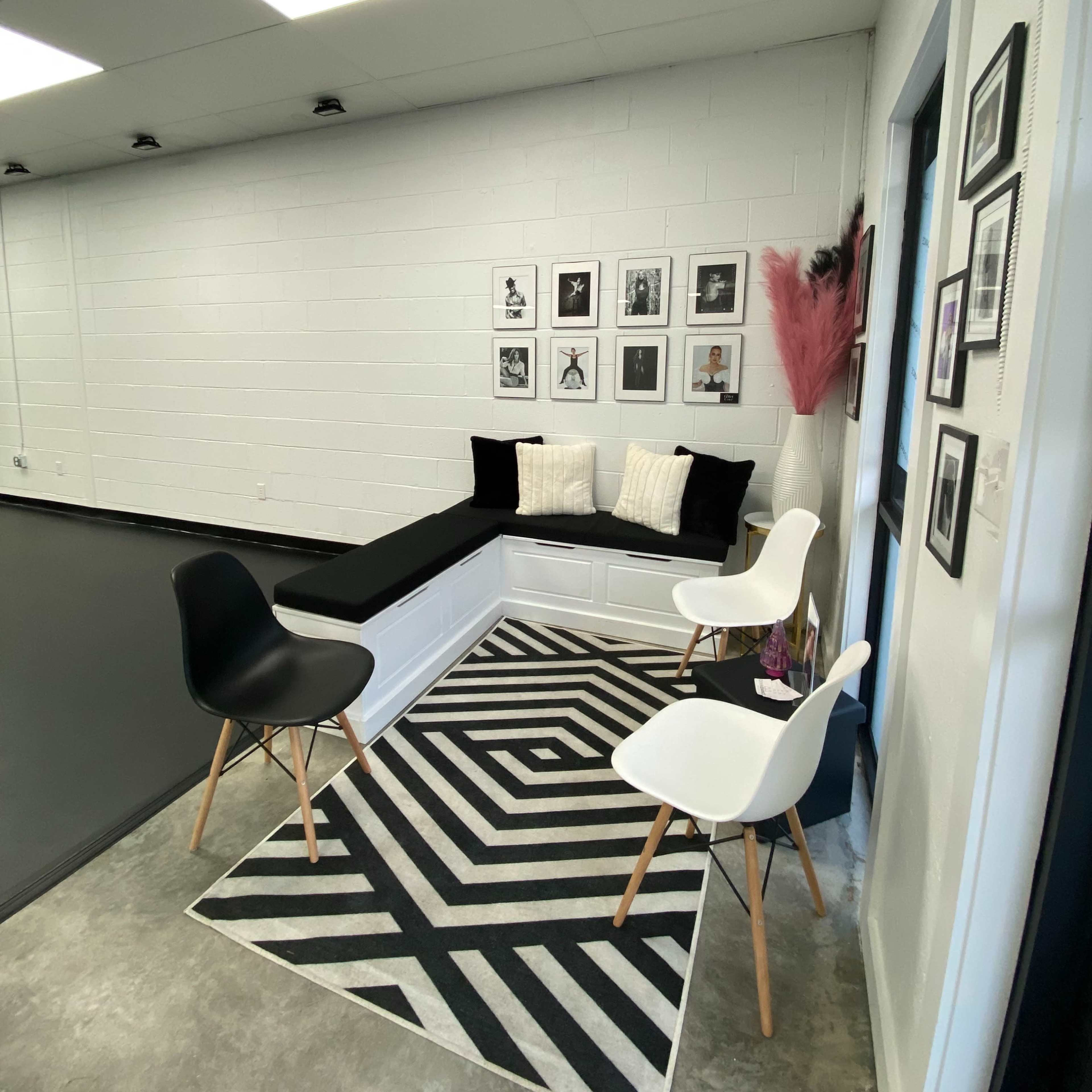 A modern interior space featuring a corner seating arrangement with a black and white striped rug, two white chairs, and framed photographs on the wall.