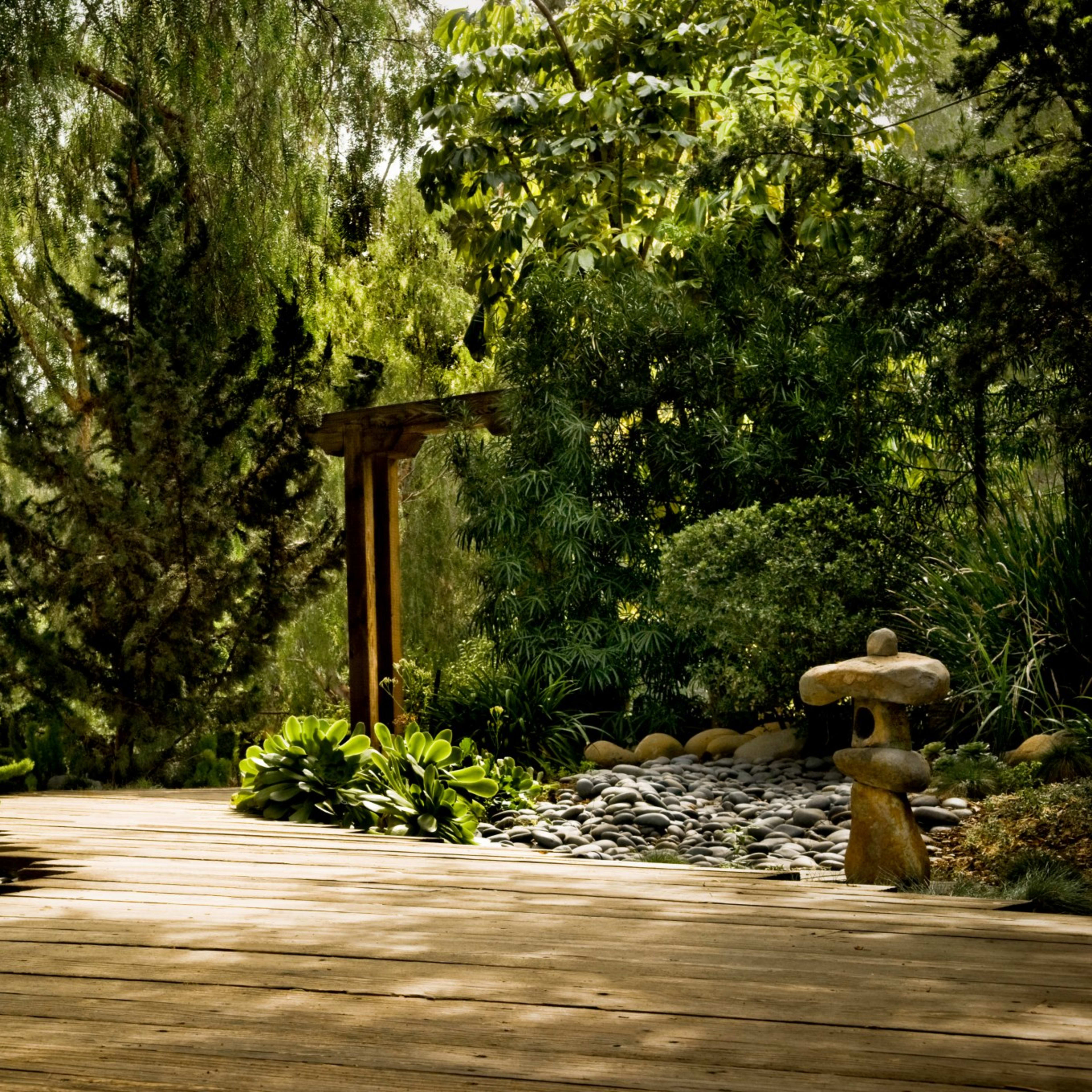 A wooden pathway leads through a landscaped garden featuring stones, lush greenery, and ornamental rocks.