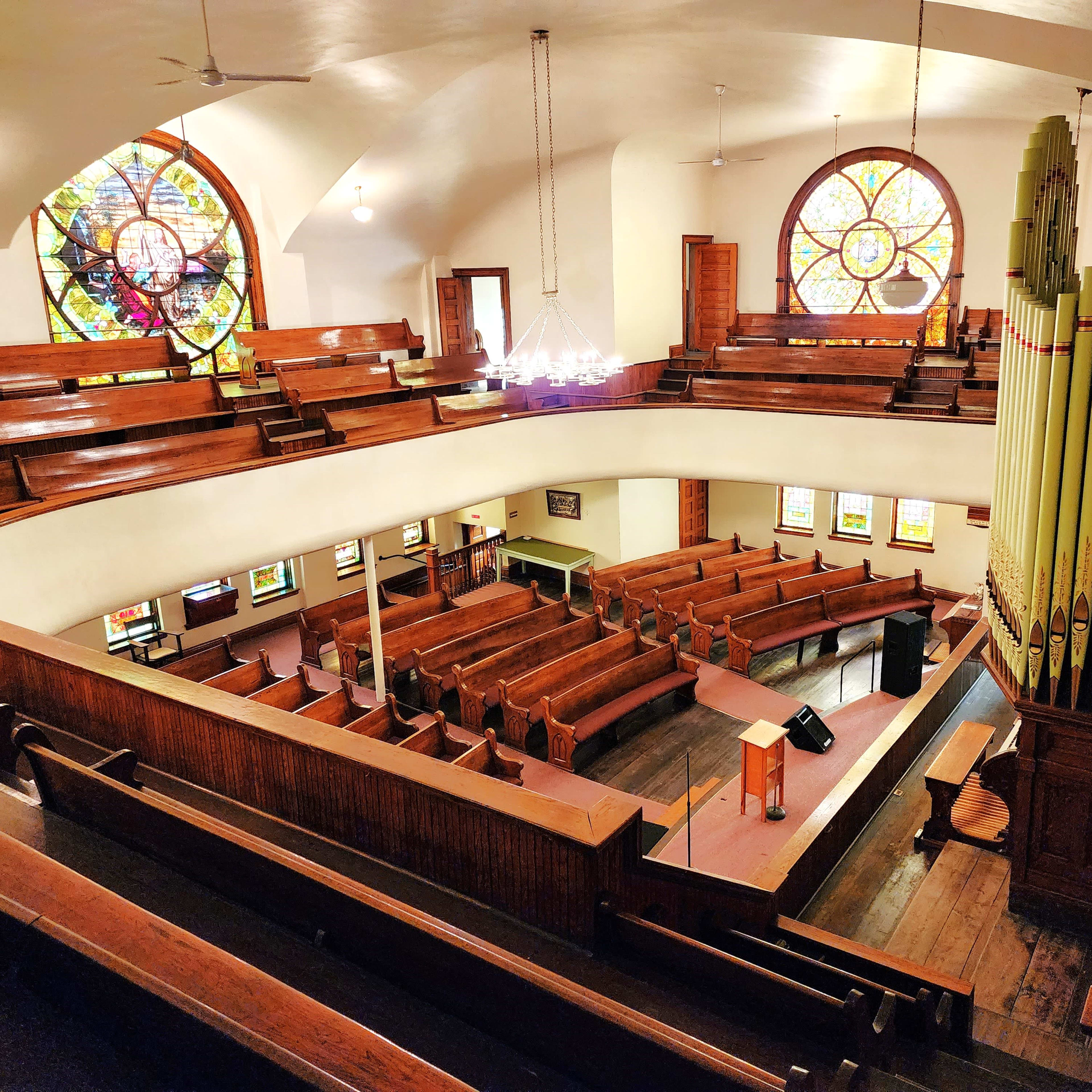 A spacious interior of a church with wooden benches, stained glass windows, and a large pipe organ on one side.
