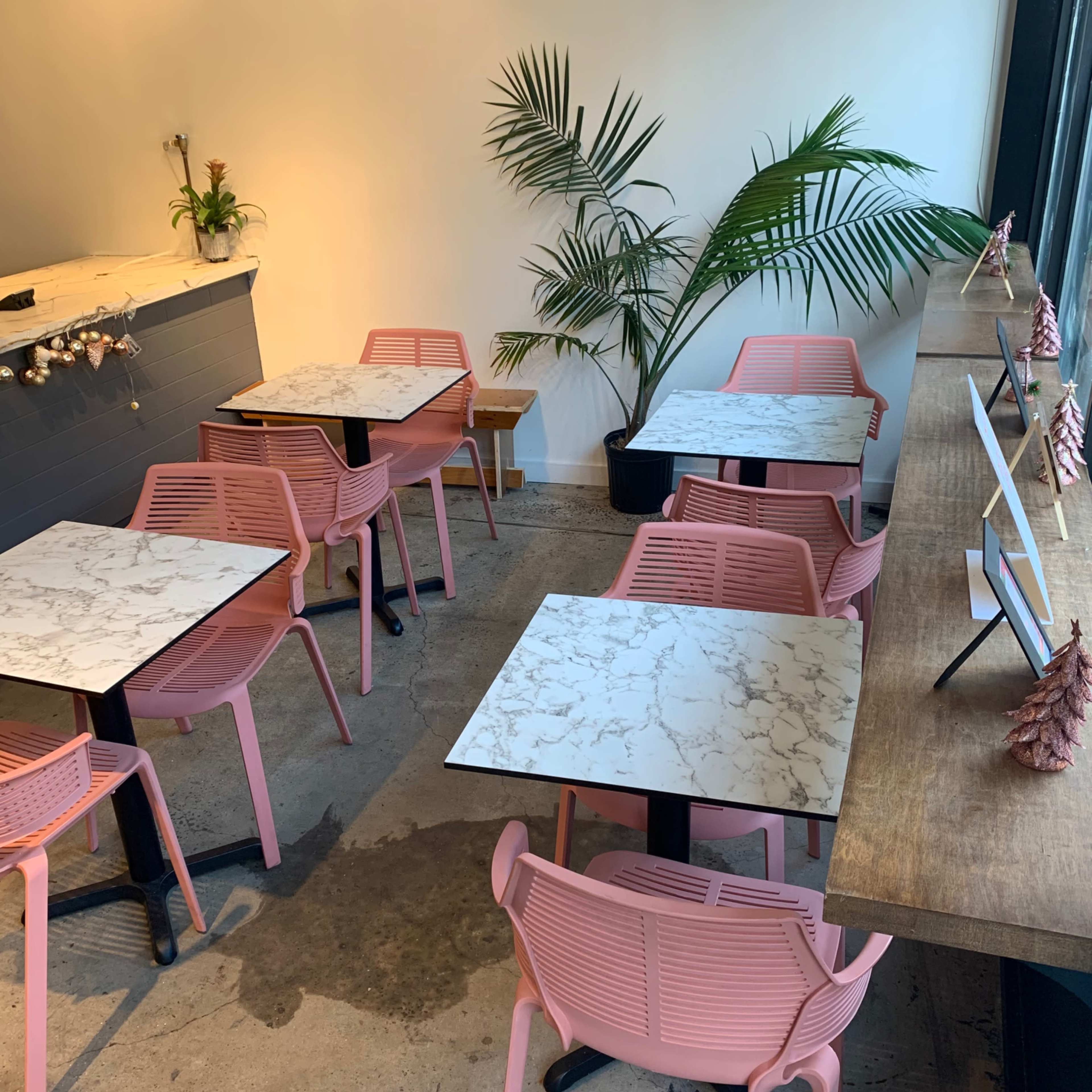 A cafe interior with pink chairs arranged around marble-top tables and a wooden counter with decorative items.