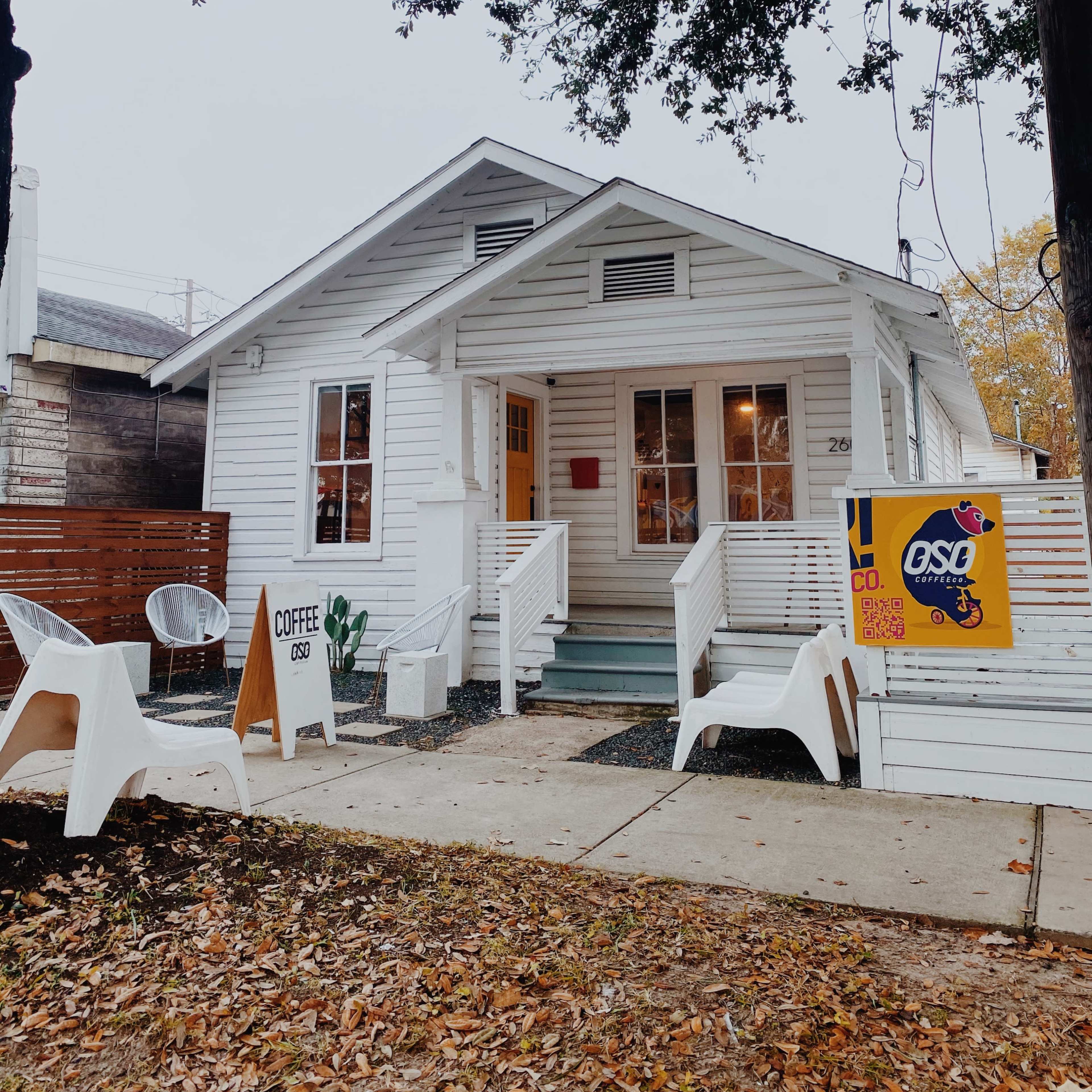 A white, single-story house with a porch features a sign advertising coffee and outdoor seating in front.