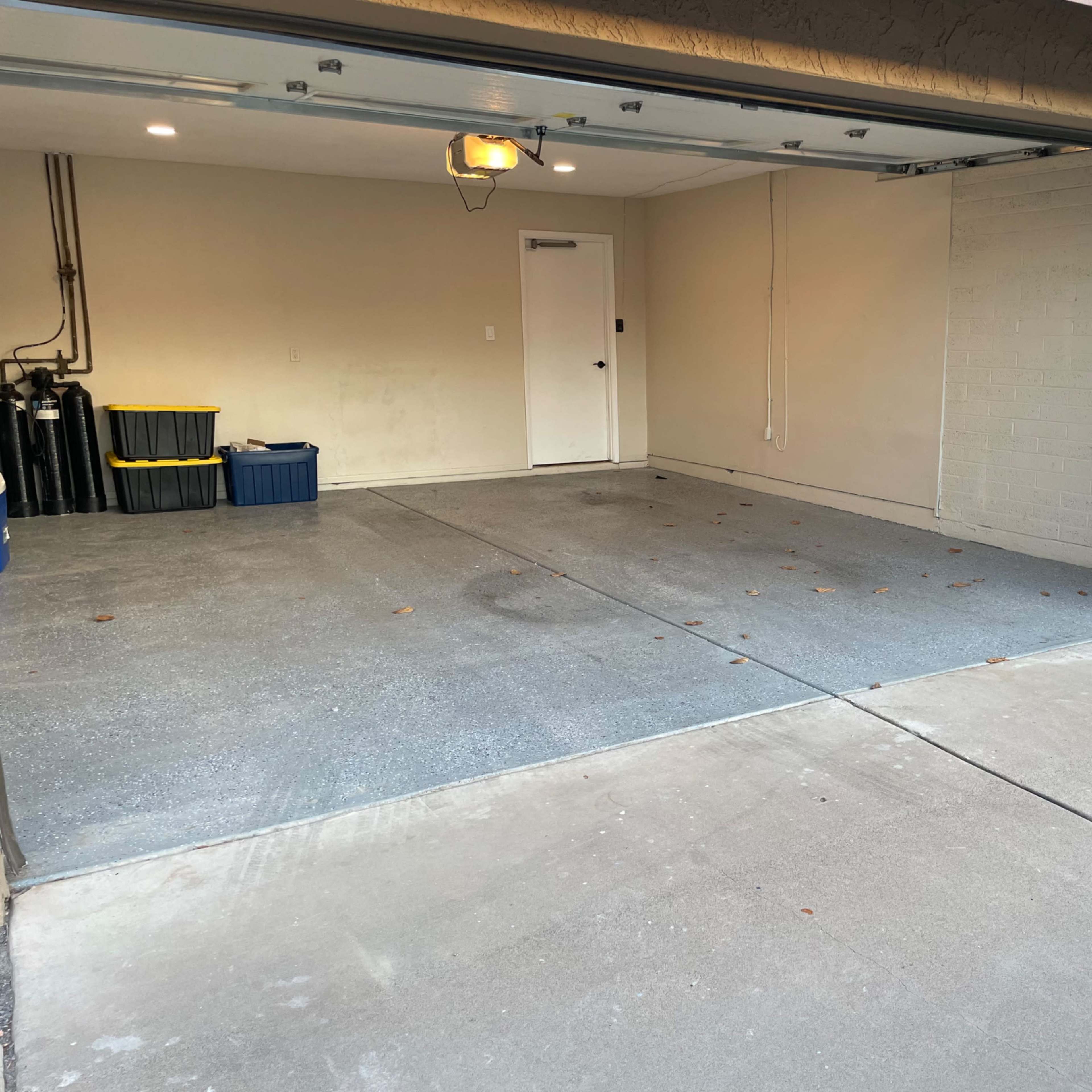 A garage with a clean, concrete floor, featuring a closed door, a storage container, and a utility area on one side.