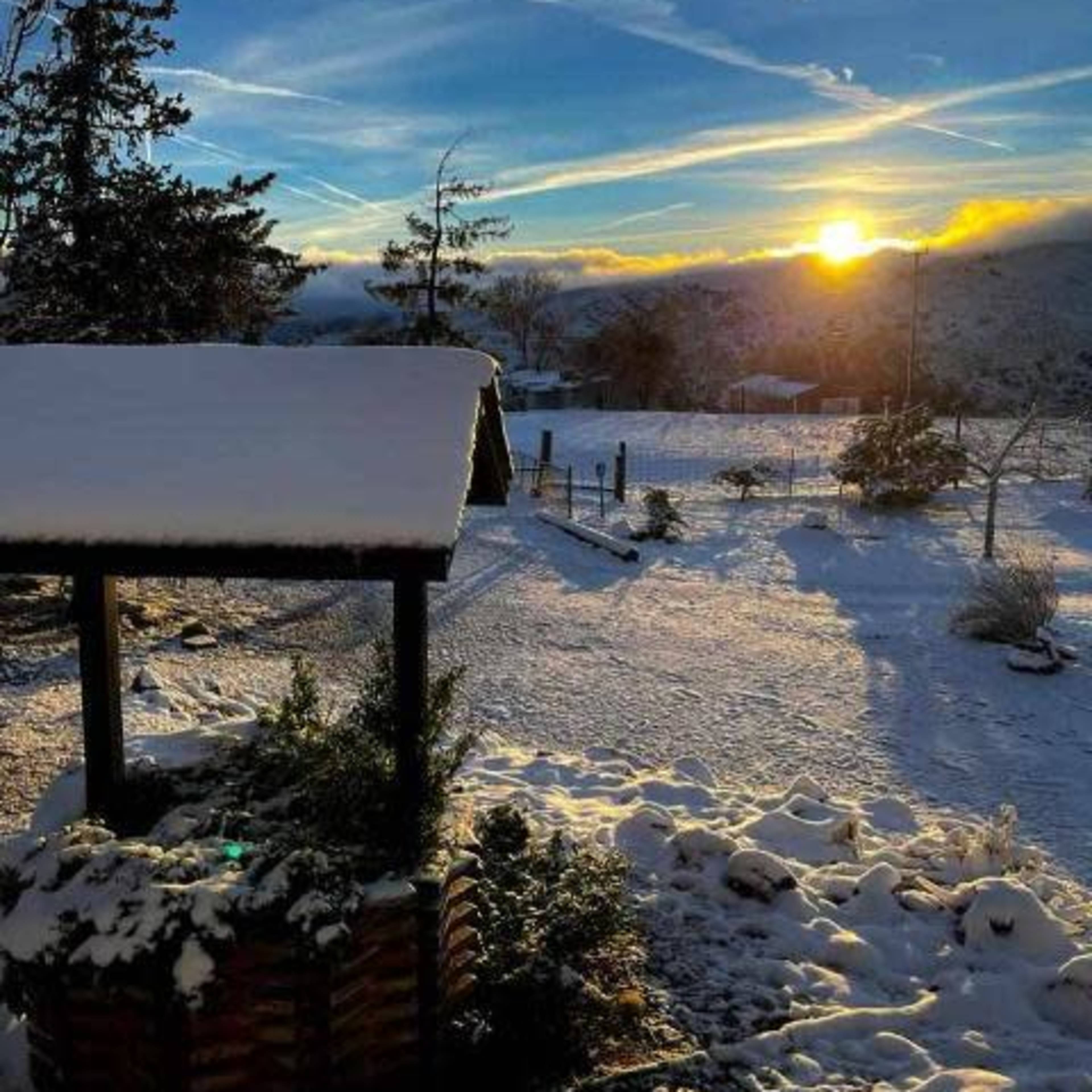 A snowy landscape with a wooden well, surrounded by trees and a rising sun in the background.