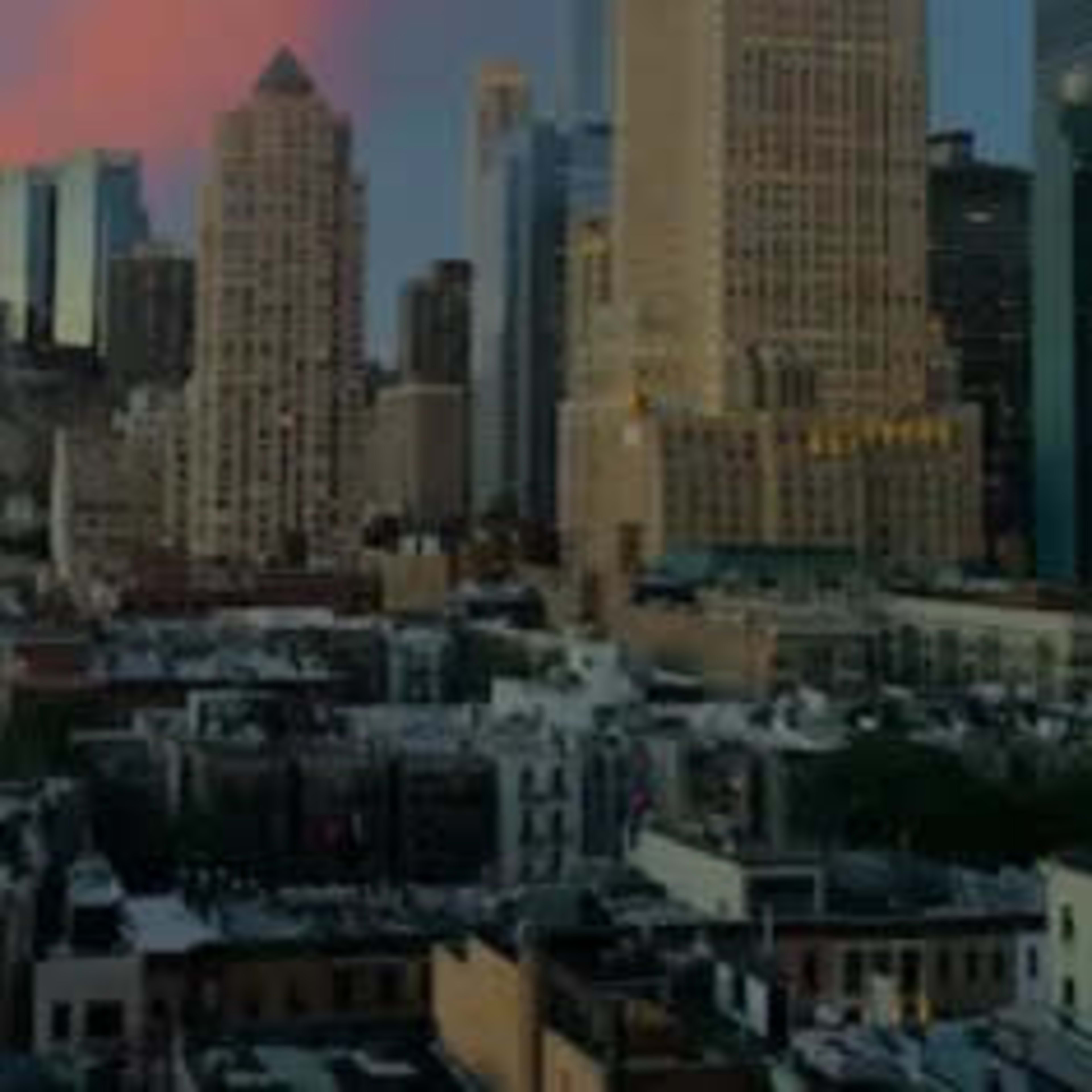 A skyline of tall buildings against a pastel sunset, with a bustling urban street below.