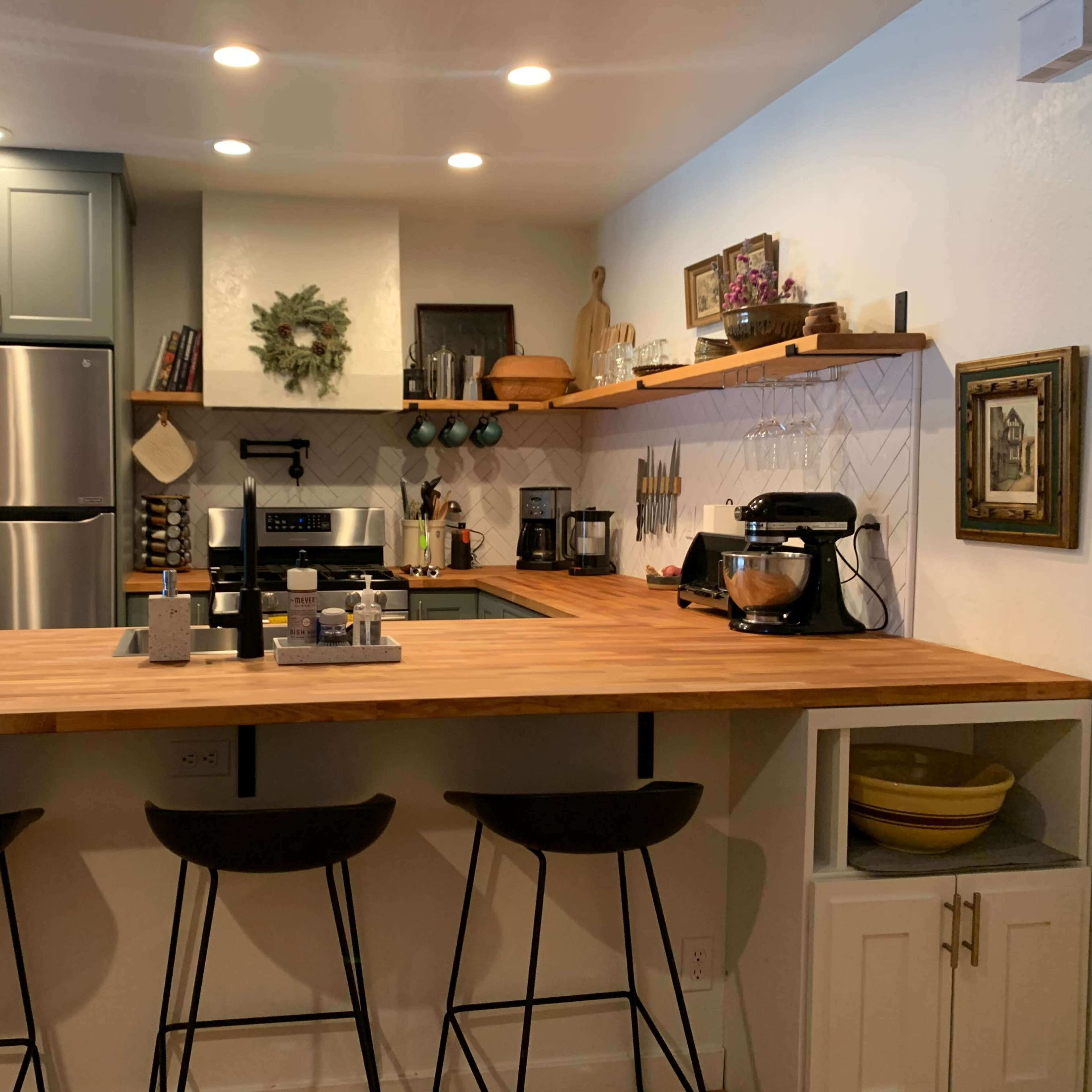 A modern kitchen with a wooden countertop, stainless steel appliances, and bar stools.