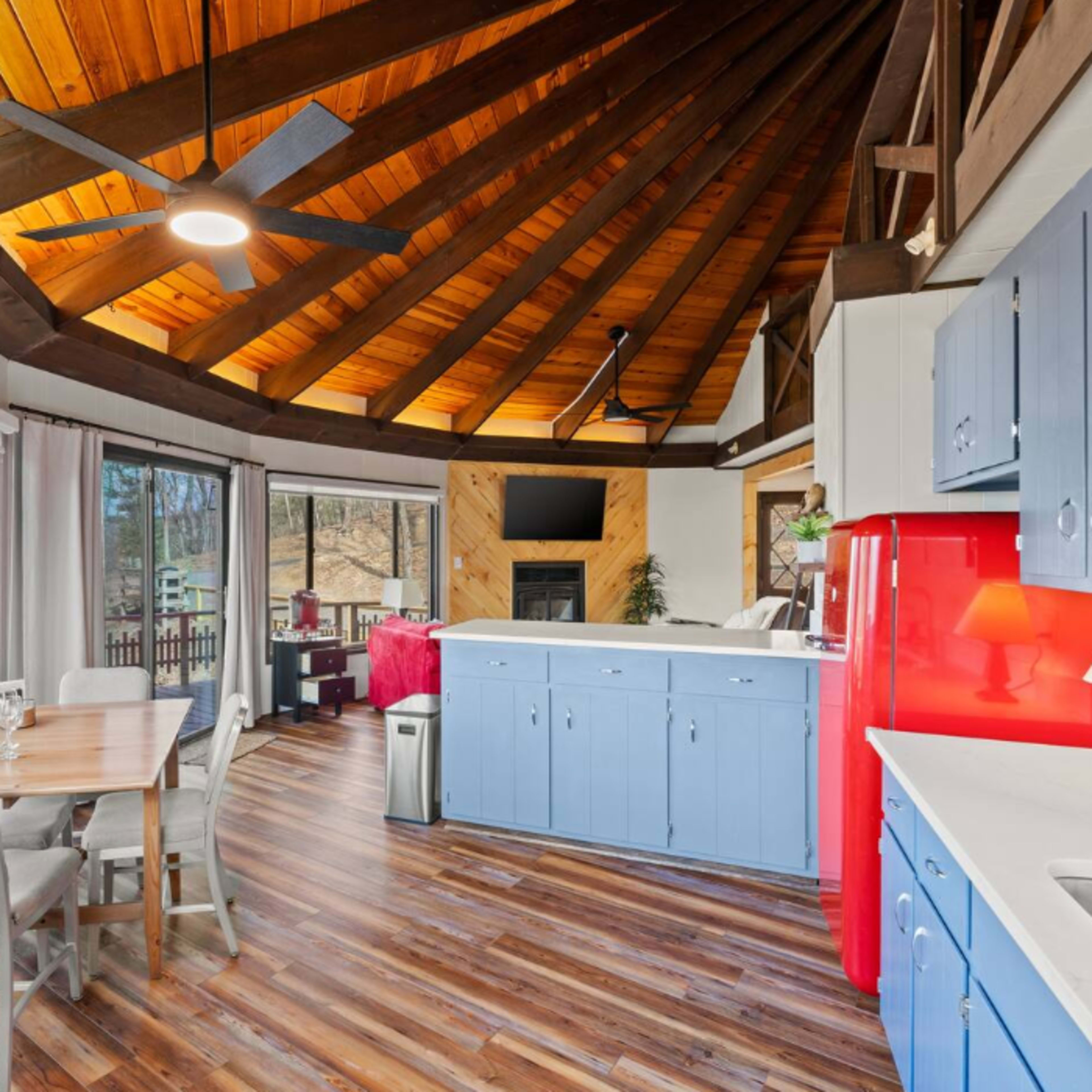 A circular kitchen and dining area with wooden beams, large windows, and a red refrigerator.
