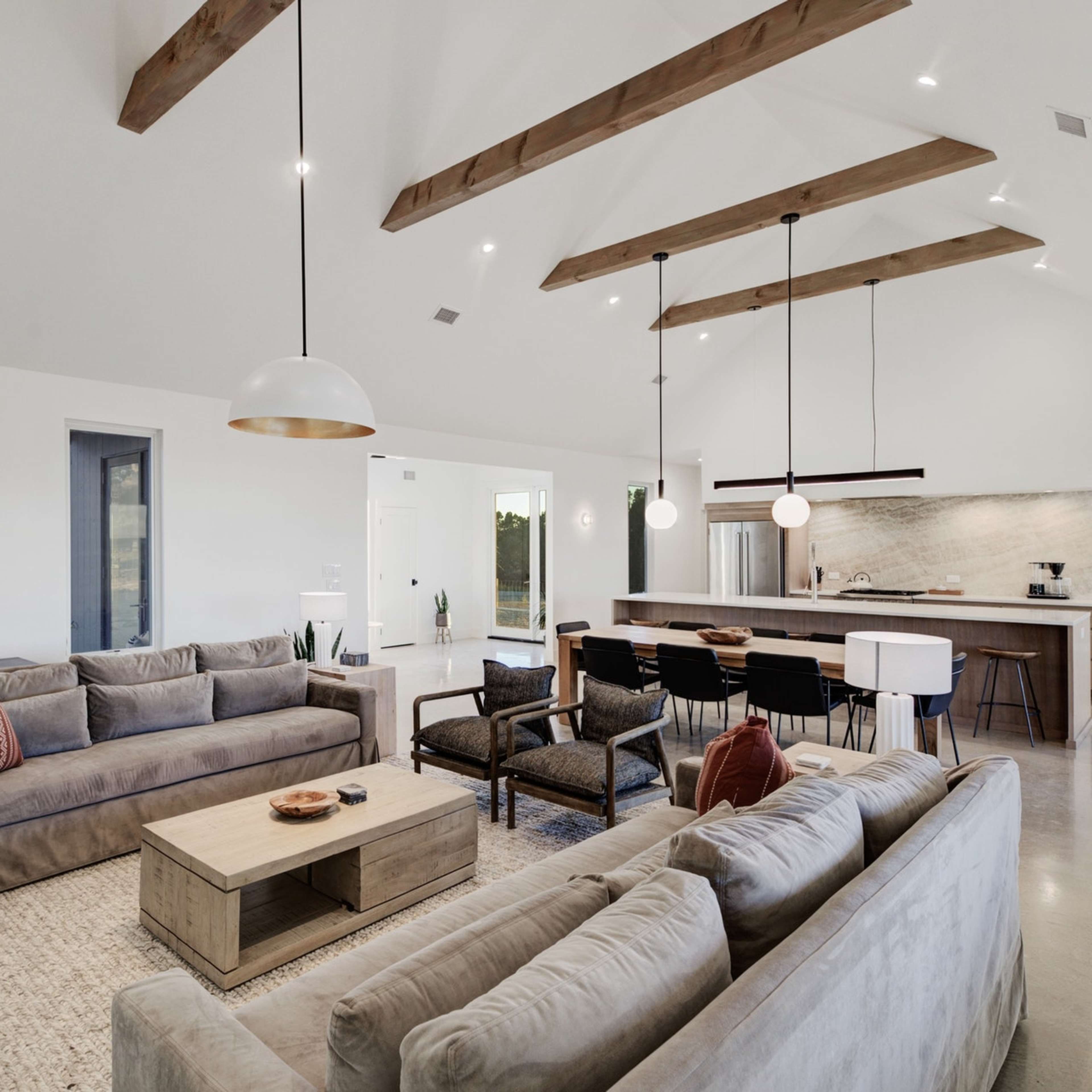 A modern living room with two large gray sofas, a coffee table, and a kitchen area in the background featuring a spacious island and bar seating.