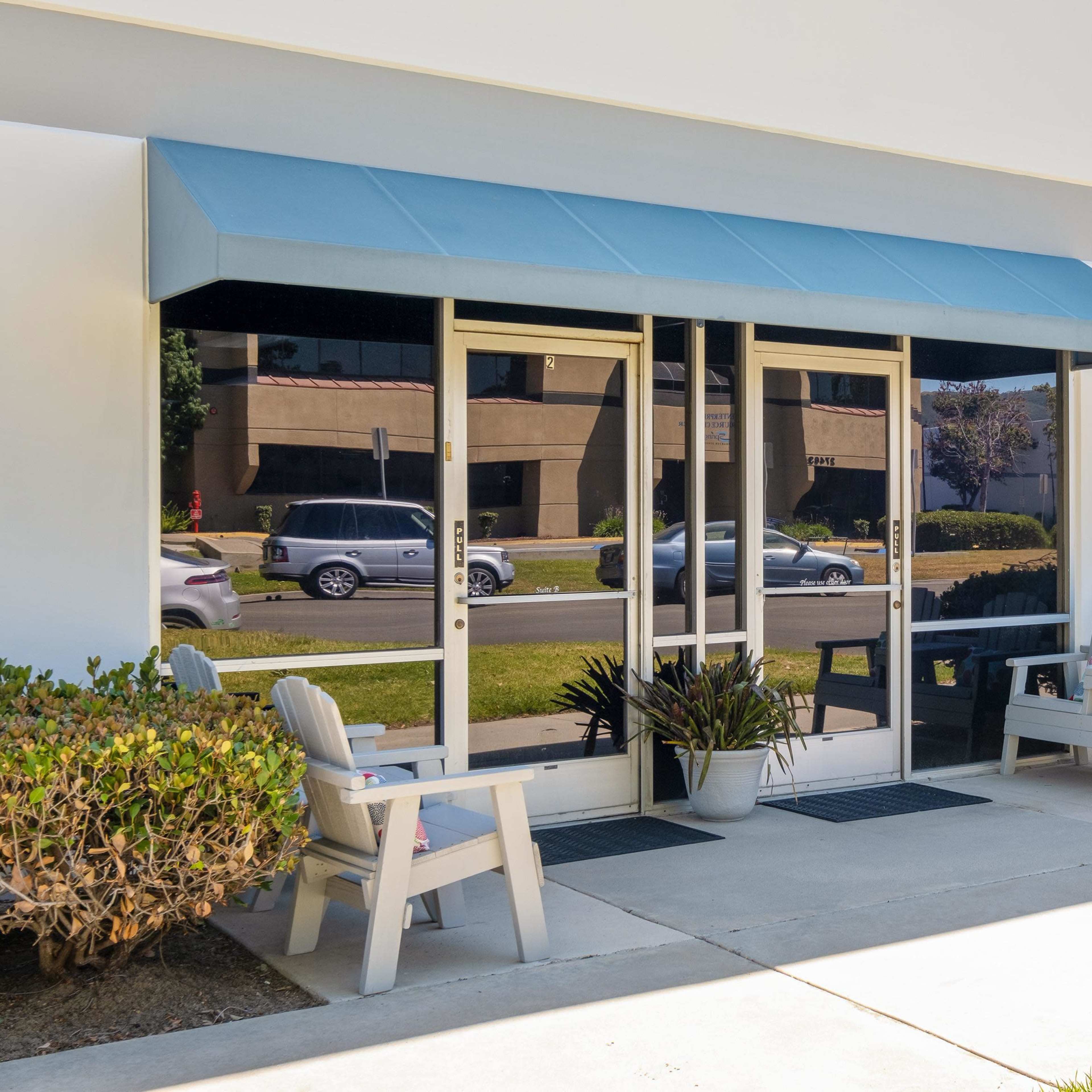 A modern meeting room with several long tables, chairs, and plants, along with a whiteboard and a blue accent wall.